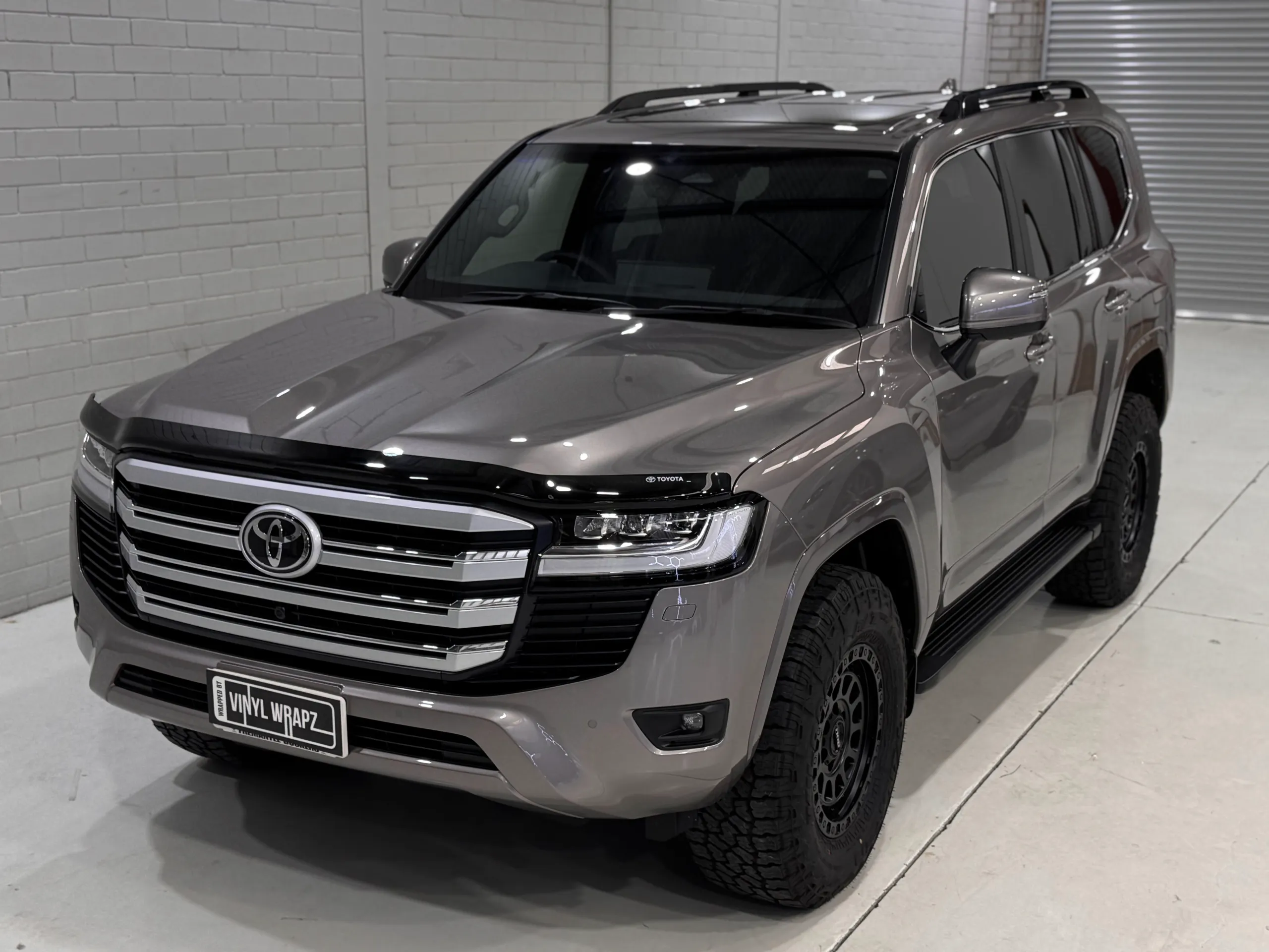 Bronze-grey Toyota LandCruiser 300 with black wheels and a gloss finish in the workshop