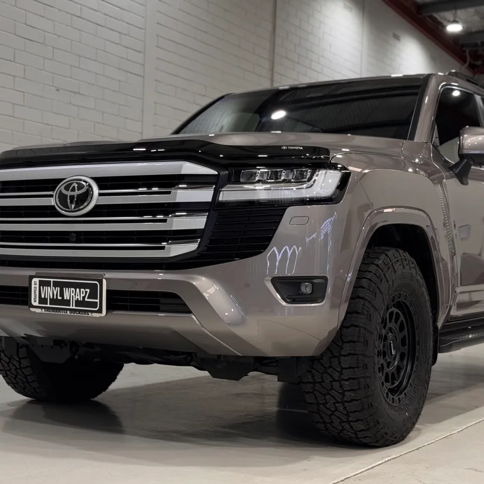 Low front-quarter view of the bronze-grey LandCruiser 300 grille, bonnet and black wheel