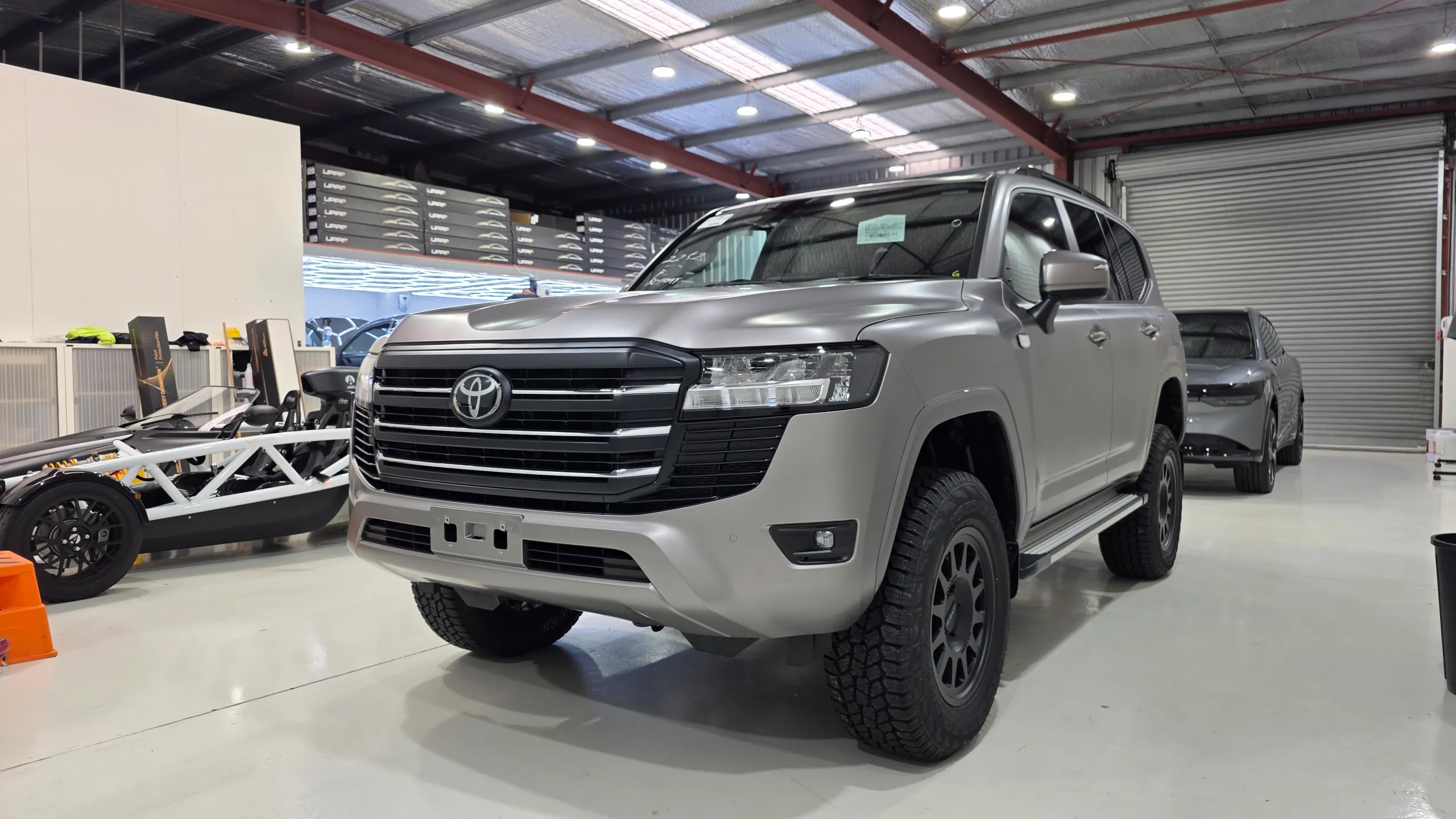 Satin bronze-grey Toyota LandCruiser 300 in the workshop with black off-road wheels