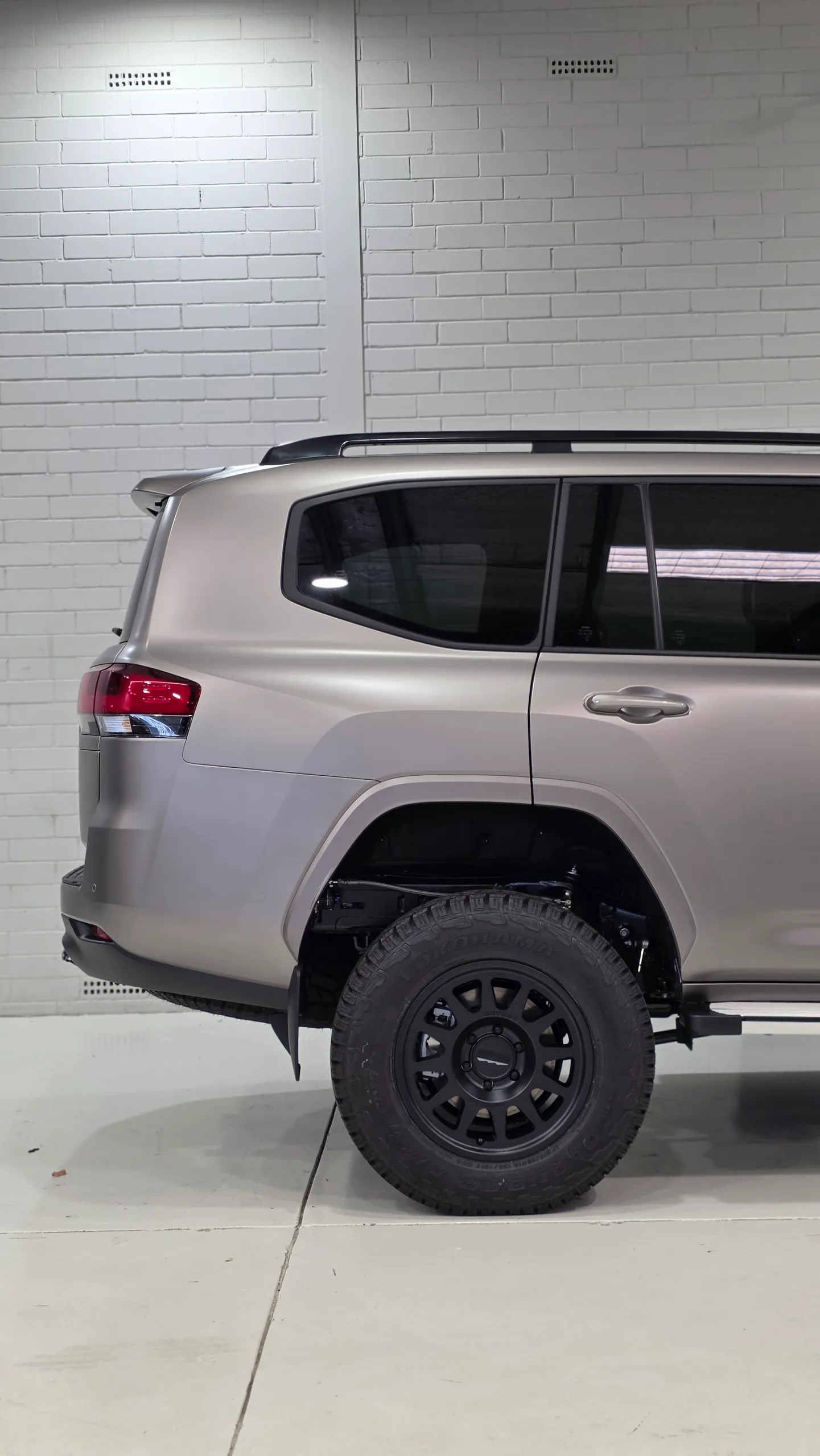 Satin bronze-grey LandCruiser 300 rear quarter and black wheel in the workshop