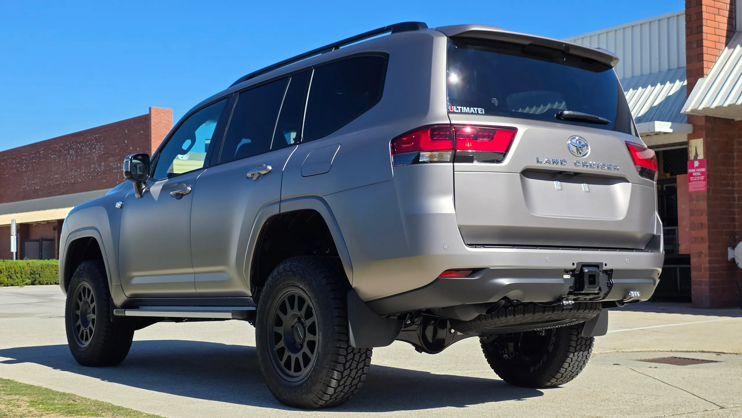 Rear-quarter view of the satin bronze-grey Toyota LandCruiser 300 outside the workshop