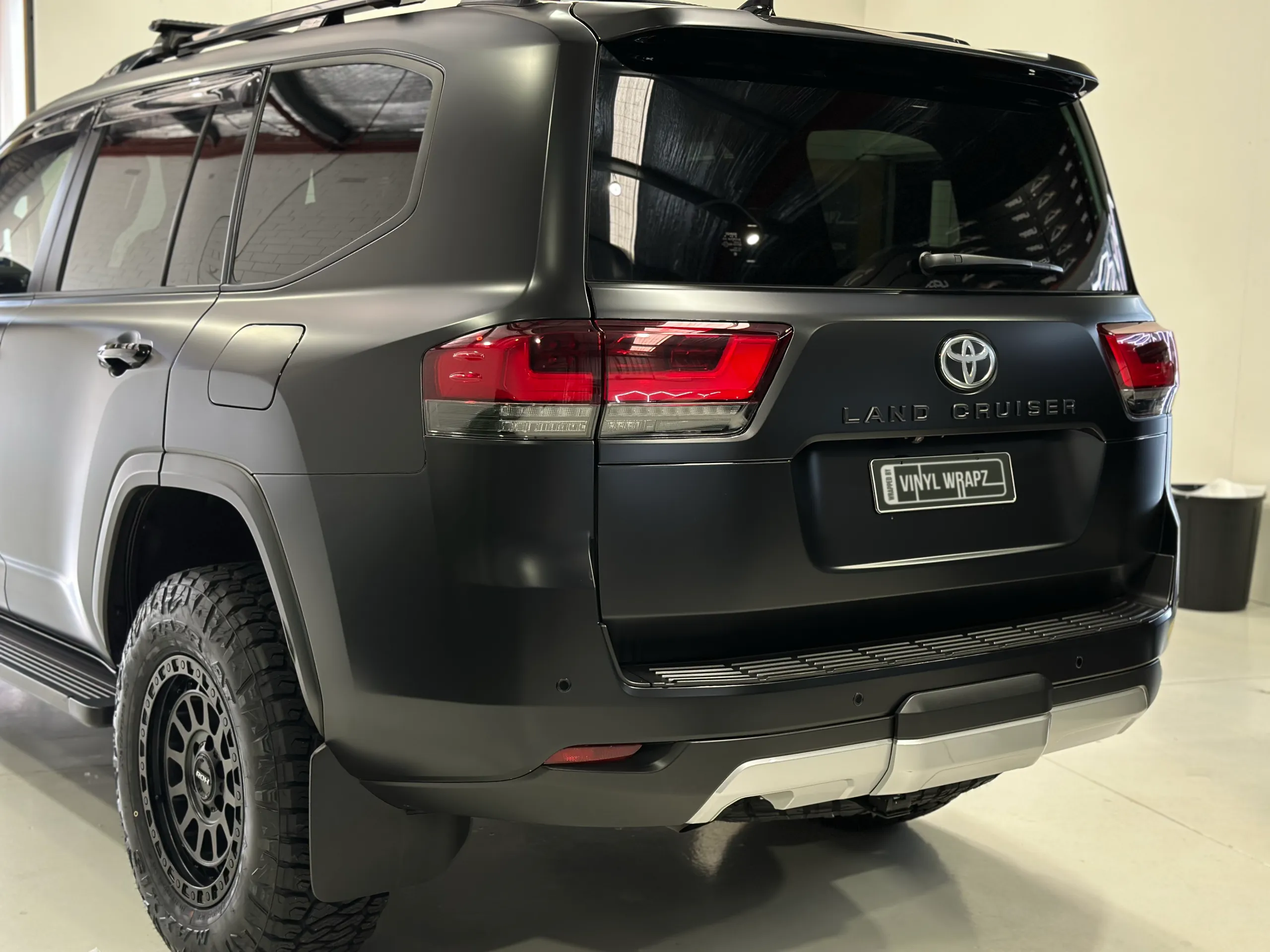 Rear-quarter view of the matte black Toyota LandCruiser 300 in the workshop