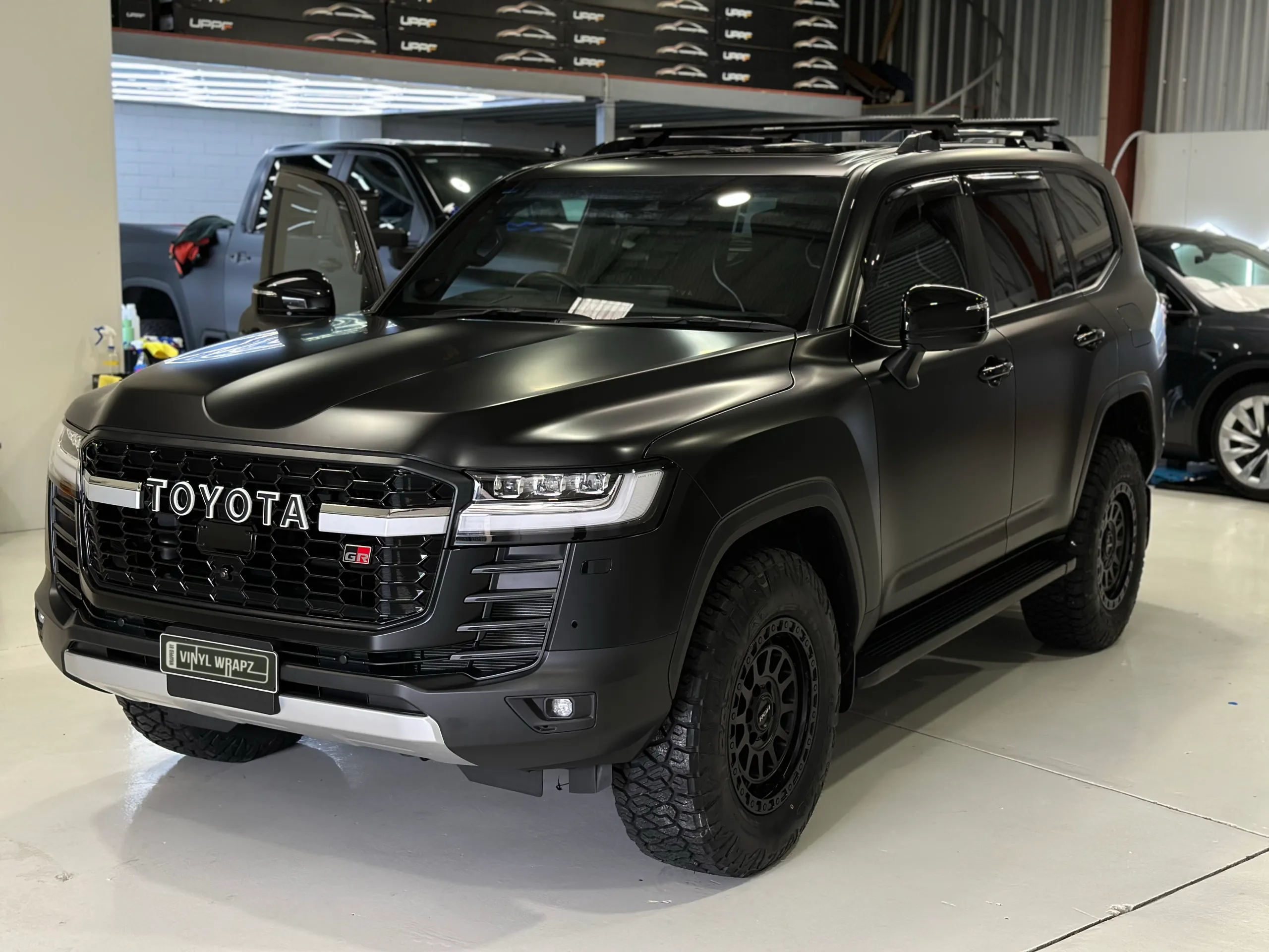 Matte black Toyota LandCruiser 300 GR Sport viewed from the front quarter with a worker in the background