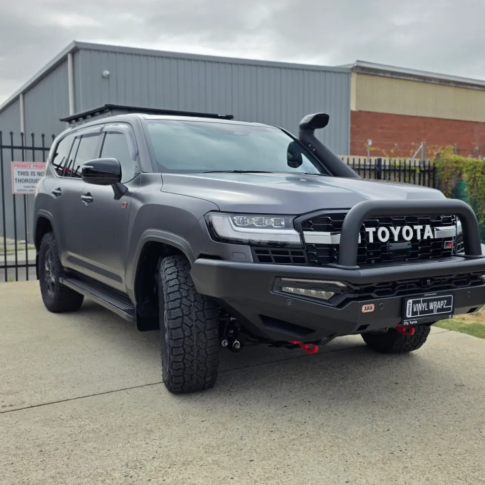 Matte grey LandCruiser 300 GR Sport with a bullbar and snorkel parked beside a fence
