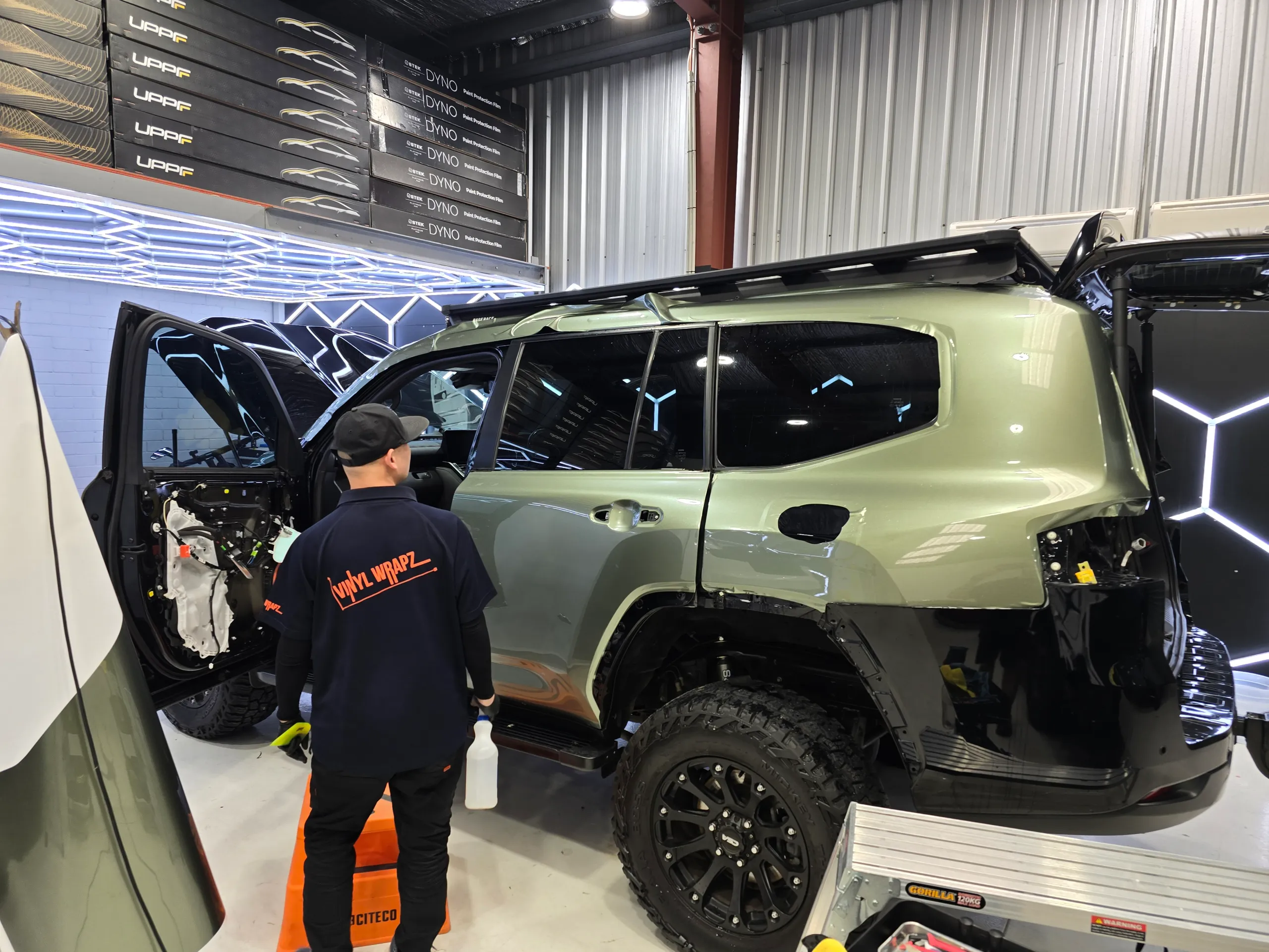 Installer facing the green LandCruiser during fitting, with door handles and rear lights removed