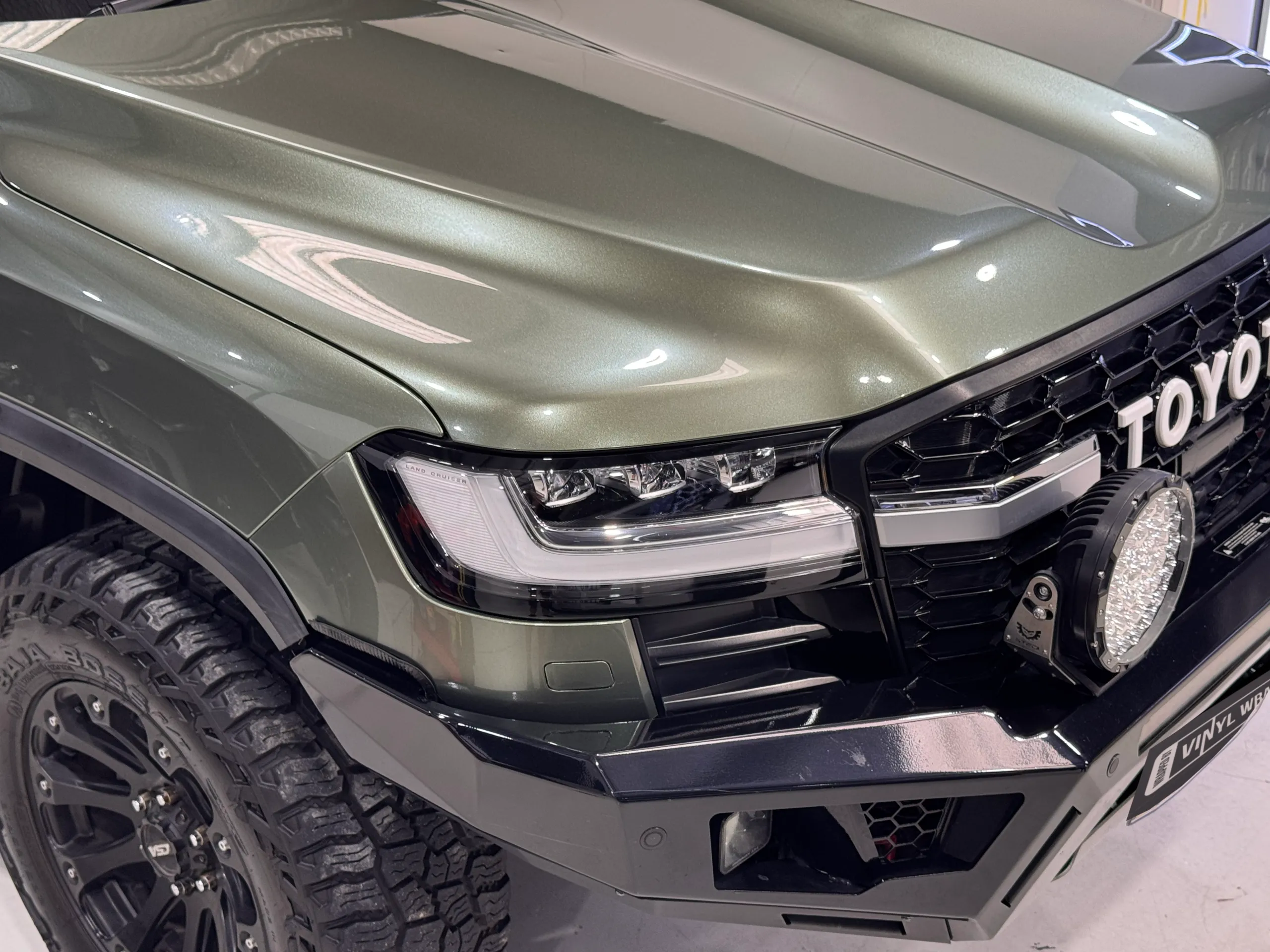 Green LandCruiser front corner with a Toyota grille and driving lights in the workshop