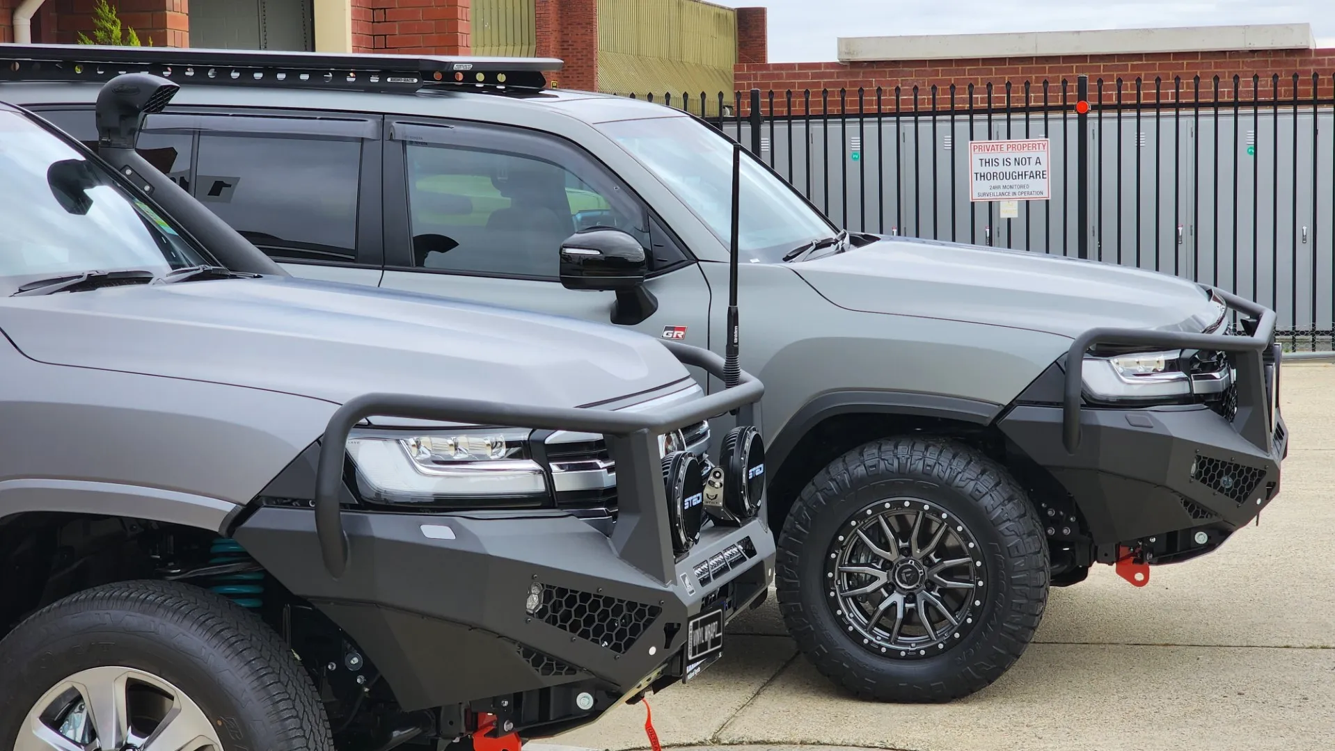 Two grey Toyota LandCruiser 300 Series vehicles with bullbars outside the workshop