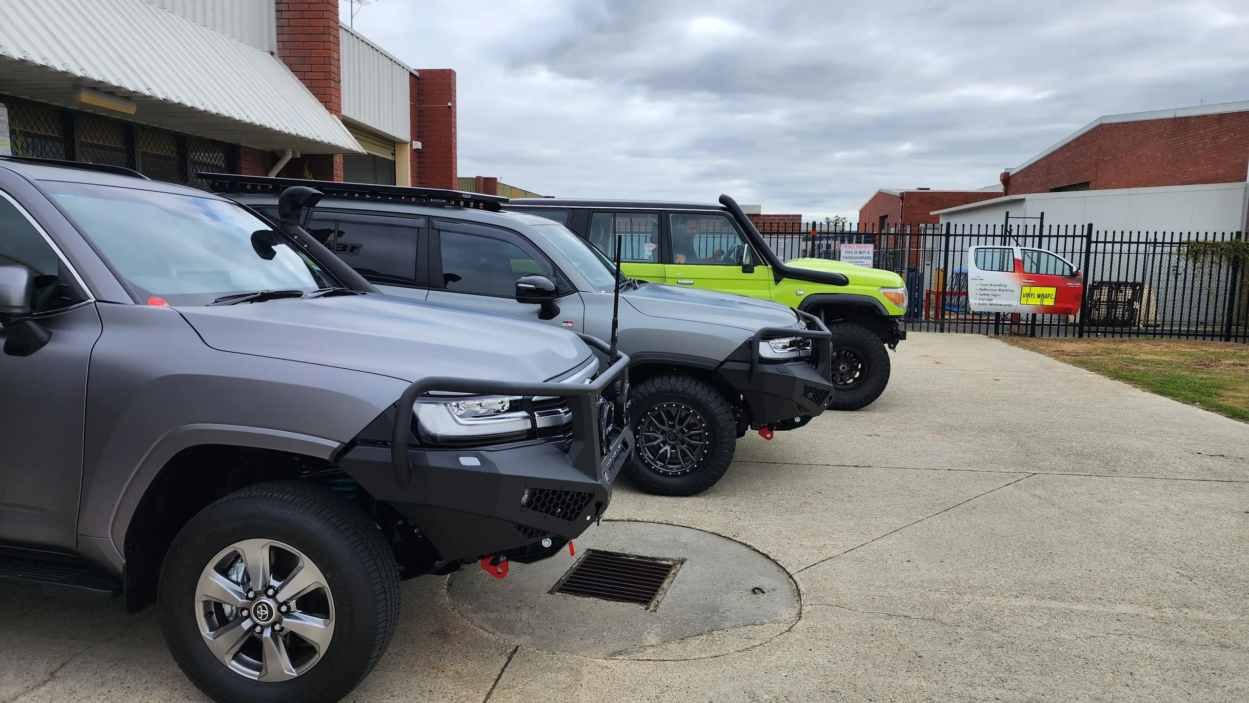 Two grey LandCruiser 300 Series vehicles and a lime green 76 Series outside the workshop