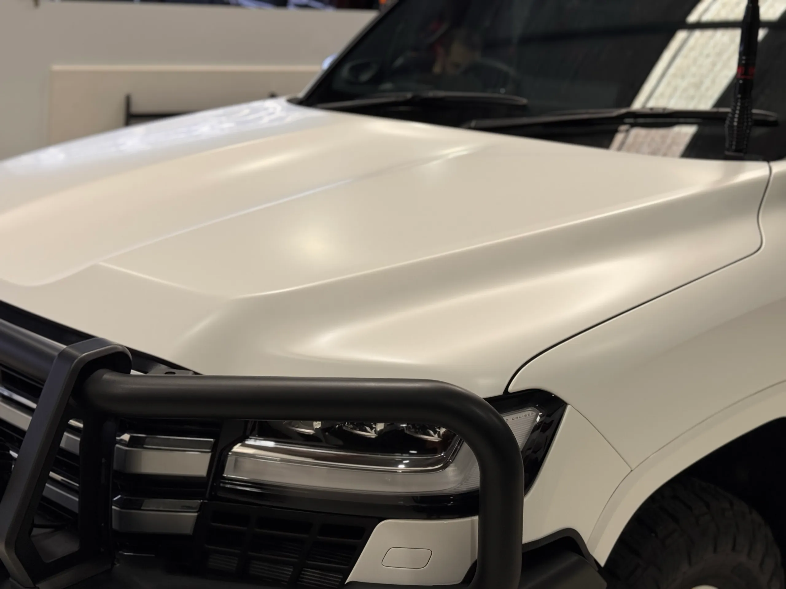 Soft reflections across the matte white Toyota LandCruiser 300 bonnet in the workshop