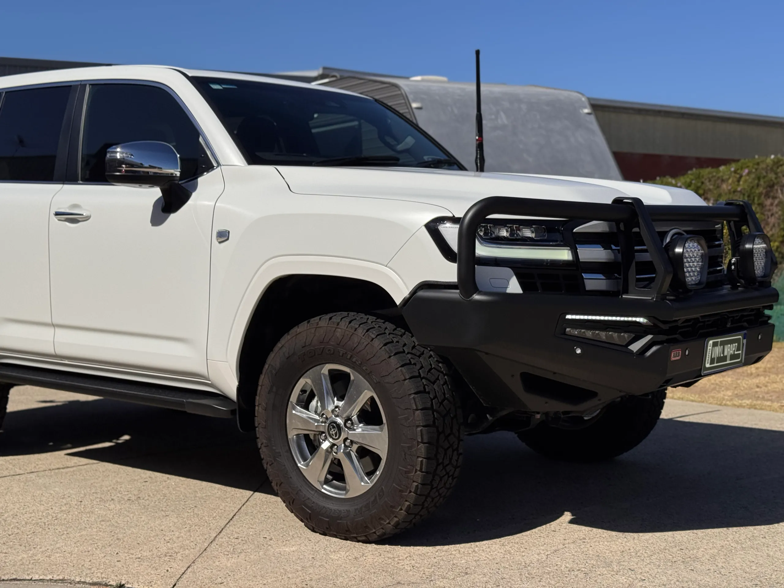 Matte white Toyota LandCruiser 300 with a black bull bar and driving lights outdoors