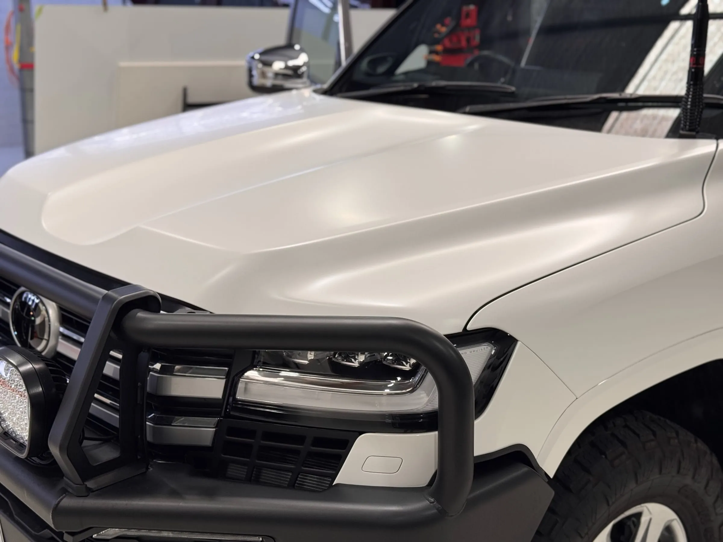 White Toyota LandCruiser 70 Series with paint protection film on the bonnet, behind a black bull bar with a driving light, Vinyl Wrapz workshop