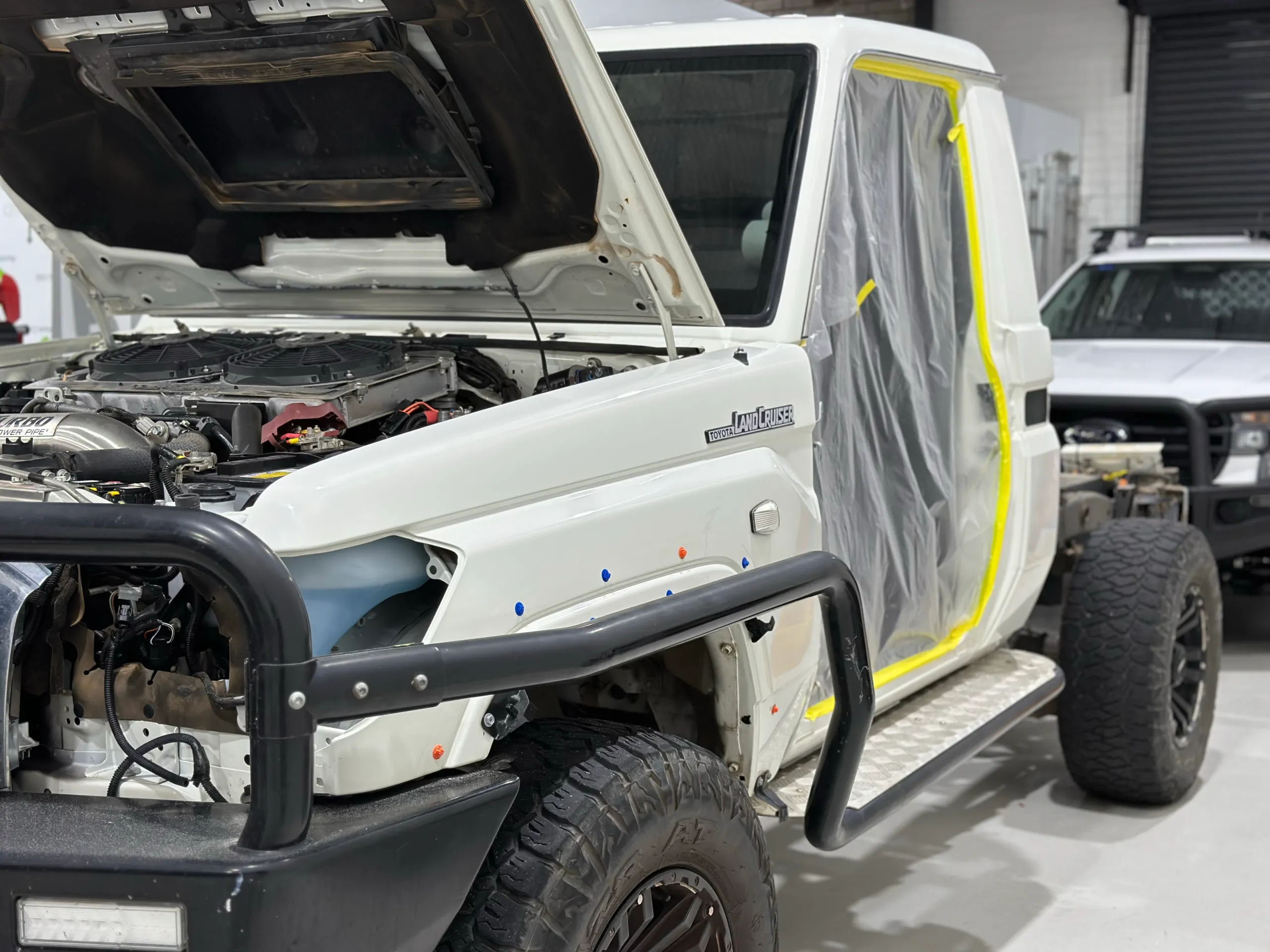 White LandCruiser cab with a door removed and its opening masked for preparation