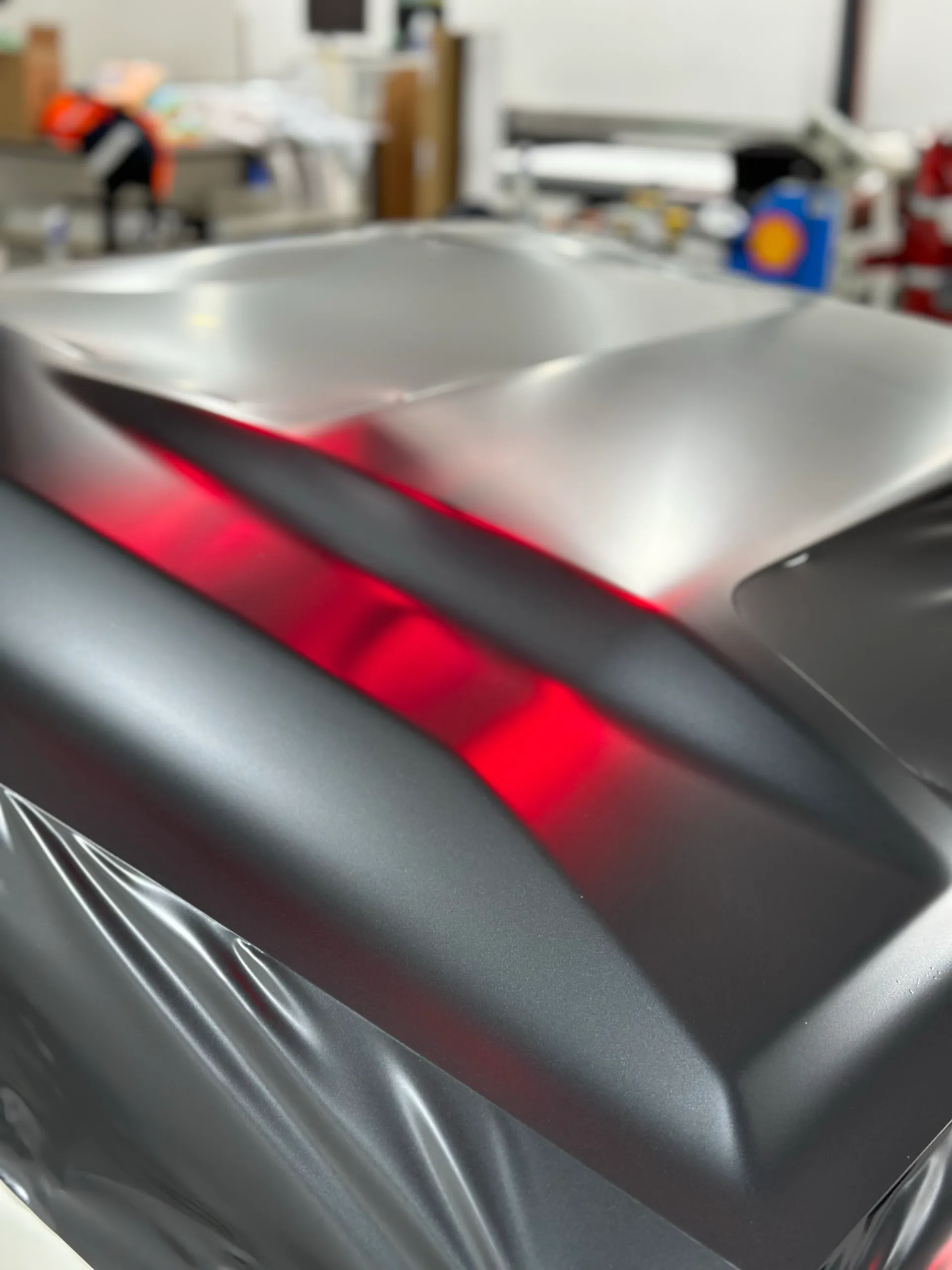 Dark grey LandCruiser bonnet reflecting red workshop heat lamps during installation