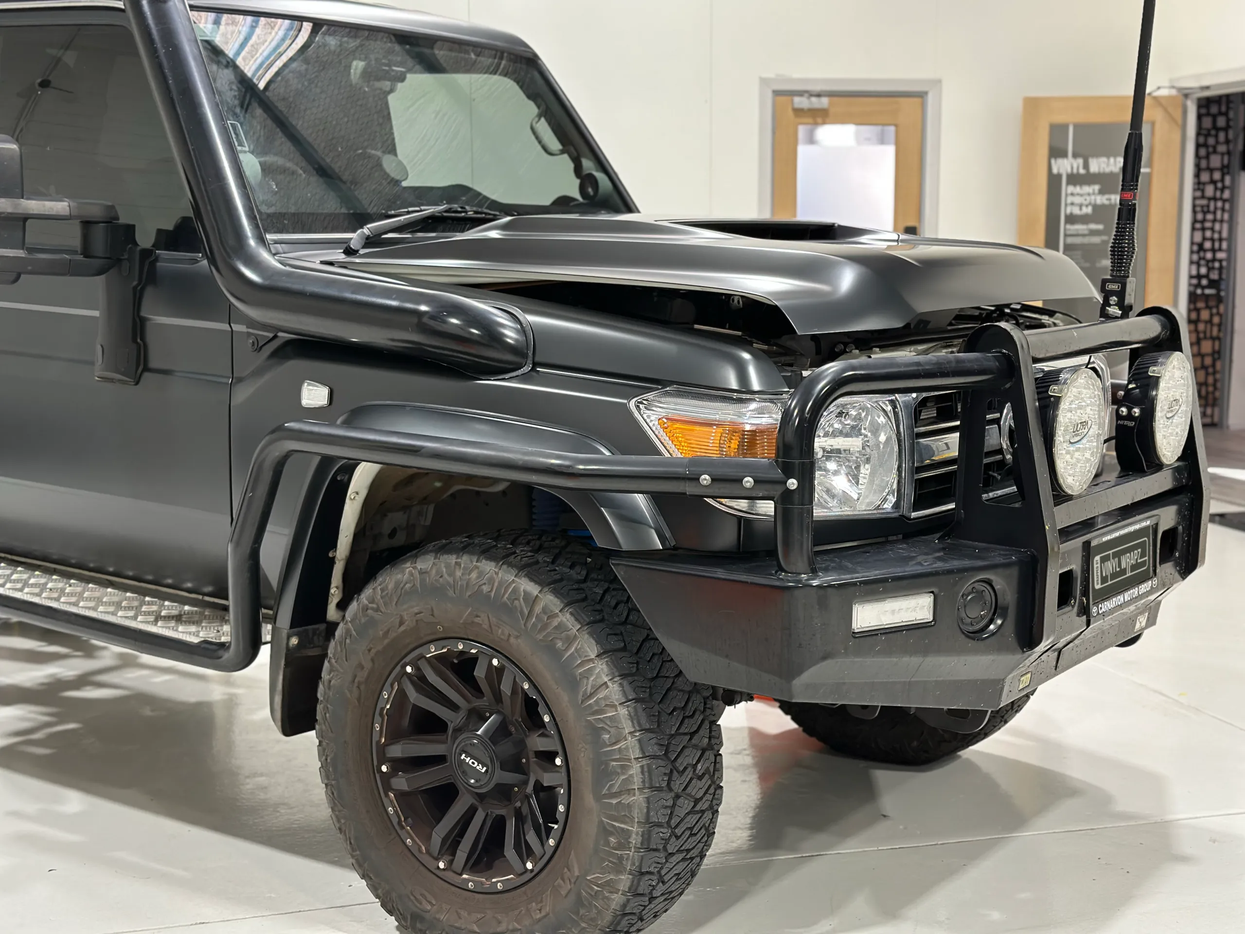 Dark grey LandCruiser front quarter with its bonnet slightly raised inside the workshop