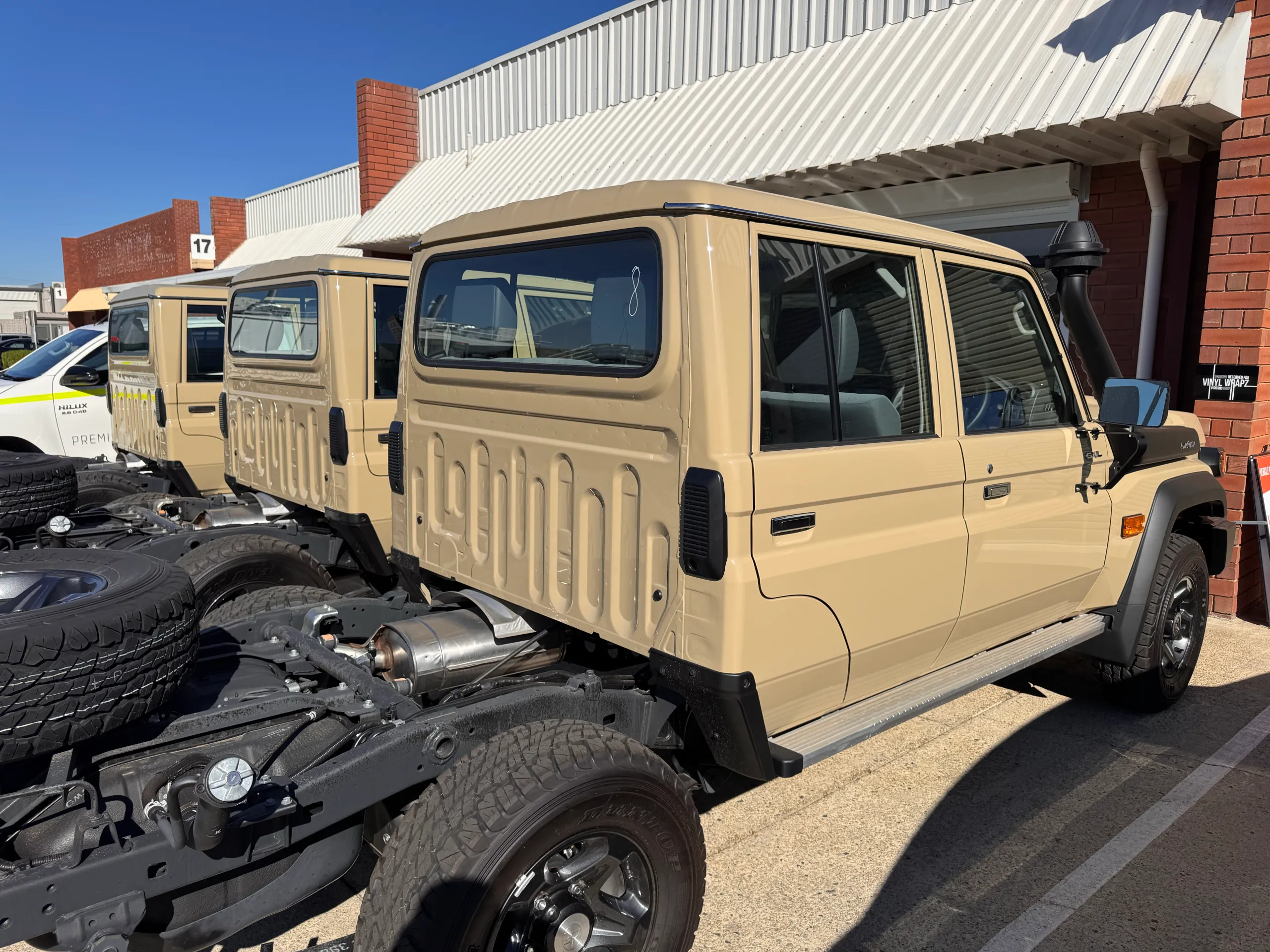 Tan LandCruiser 79 double-cab chassis vehicles with exposed rear chassis outside the workshop