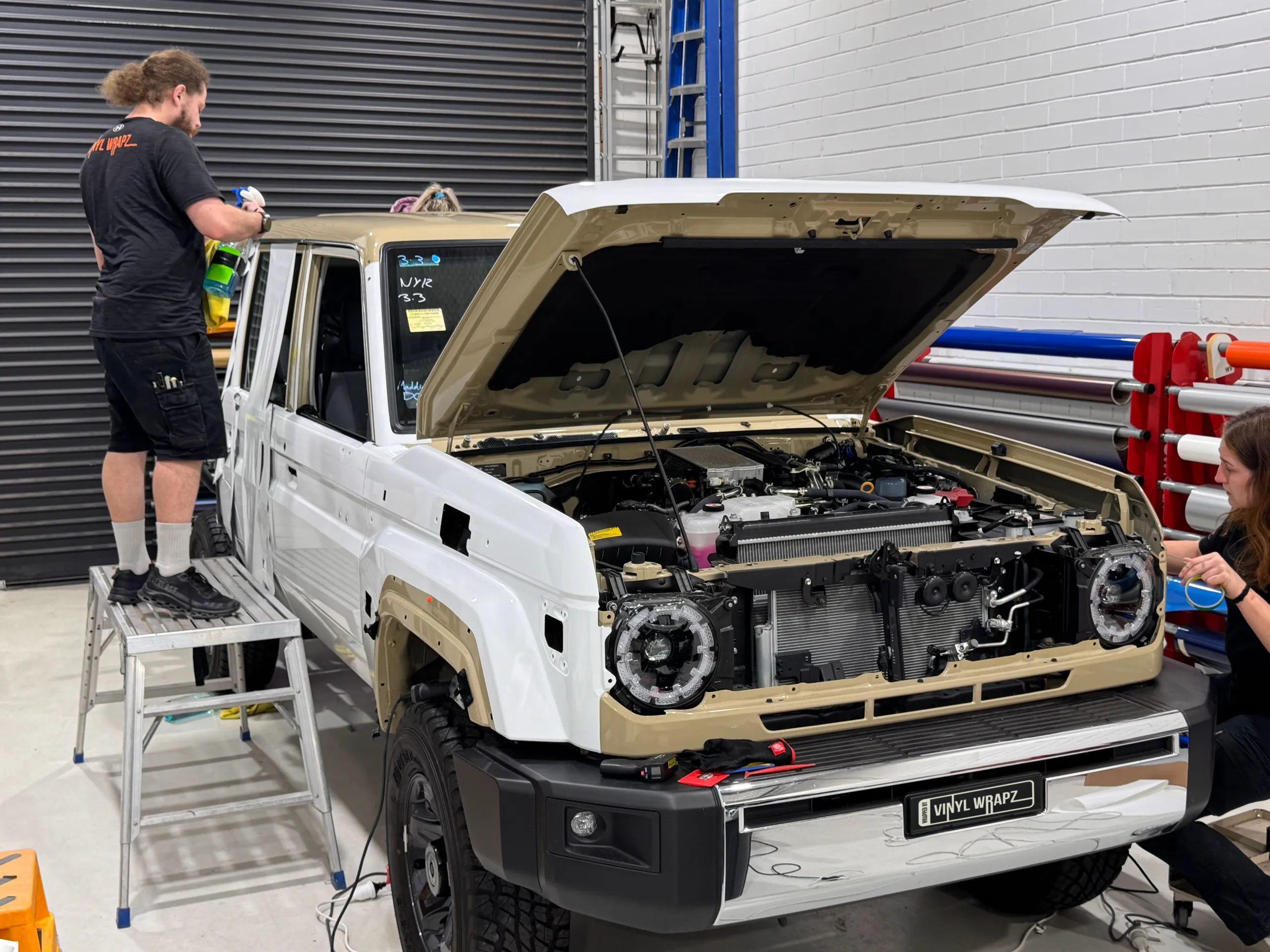 Installers wrapping a LandCruiser 79 in white with the bonnet open and front trim removed
