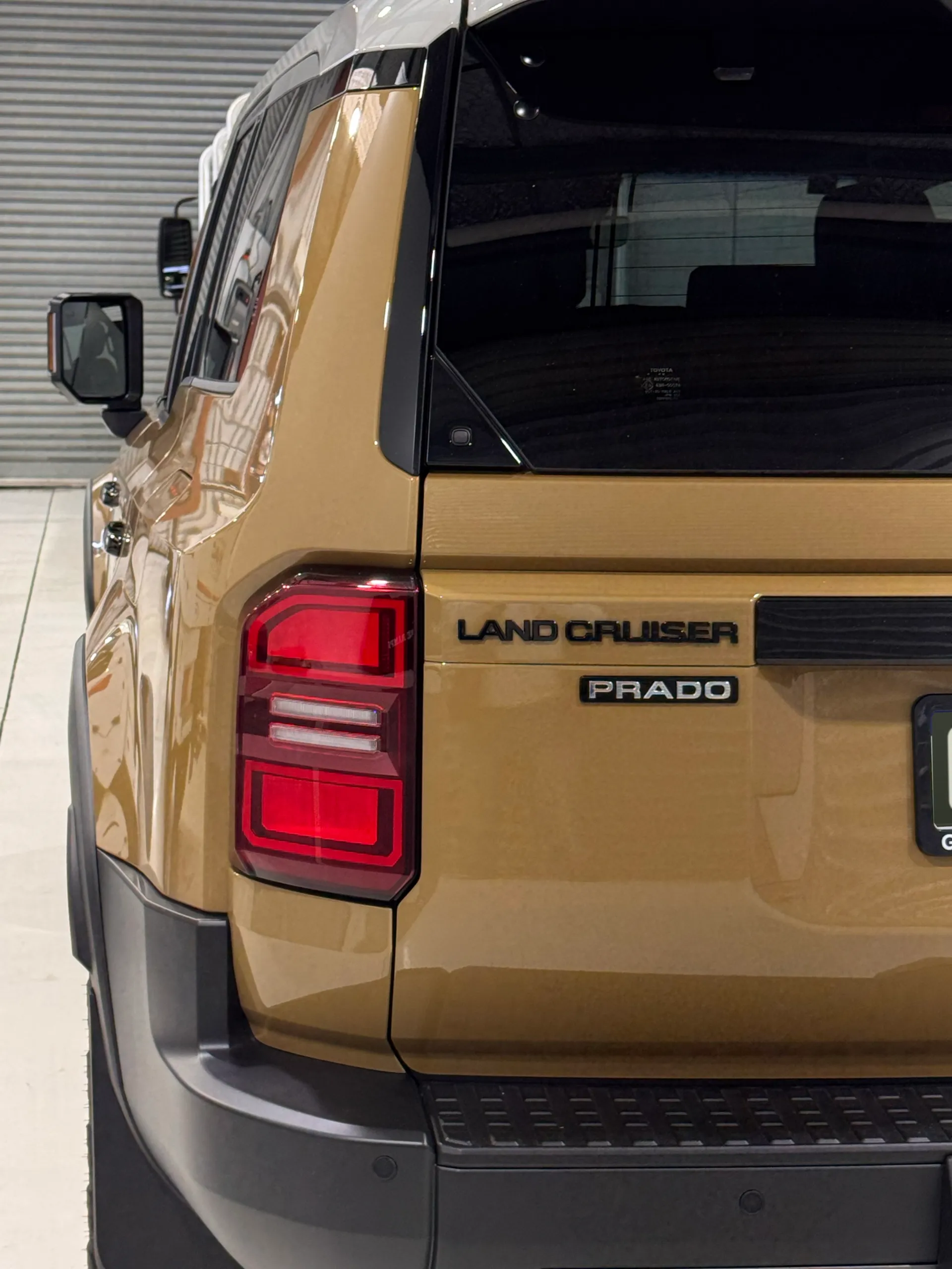 Toyota LandCruiser Prado rear light and gold tailgate beside its black window trim