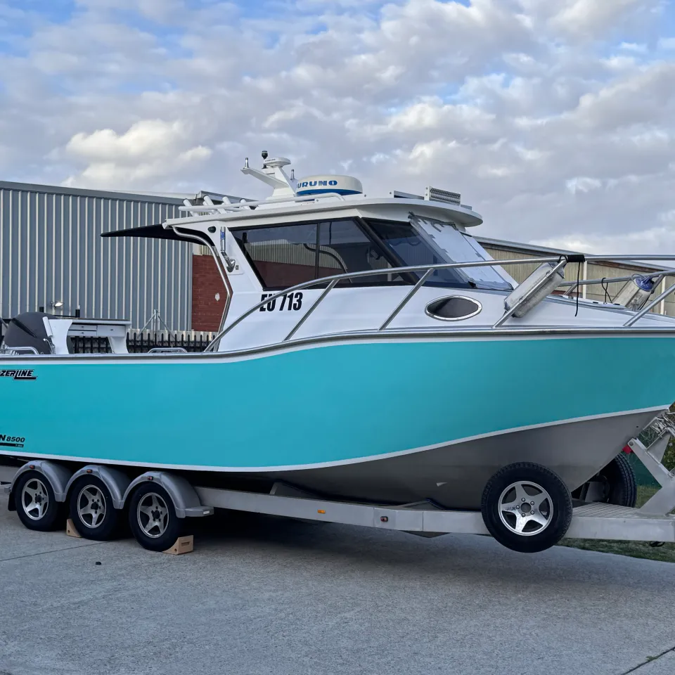 Turquoise Razerline Olympian hull on a triple-axle trailer outside the workshop