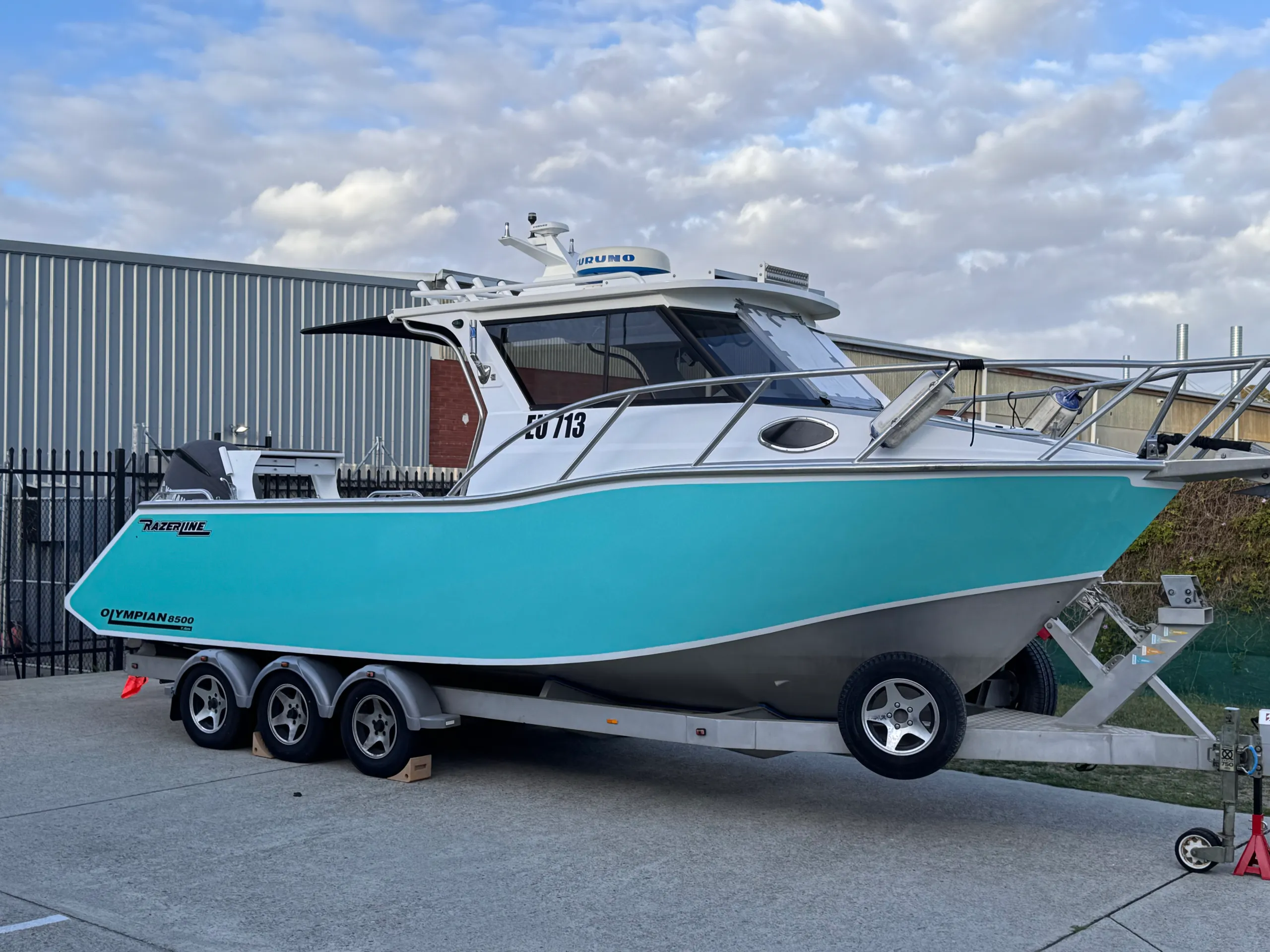 Turquoise Razerline Olympian hull on a triple-axle trailer outside the workshop