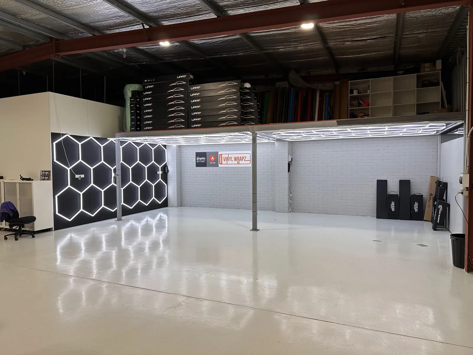 Wide view of the Vinyl Wrapz workshop bays in Osborne Park under hexagon LED lighting, with film rolls stored above