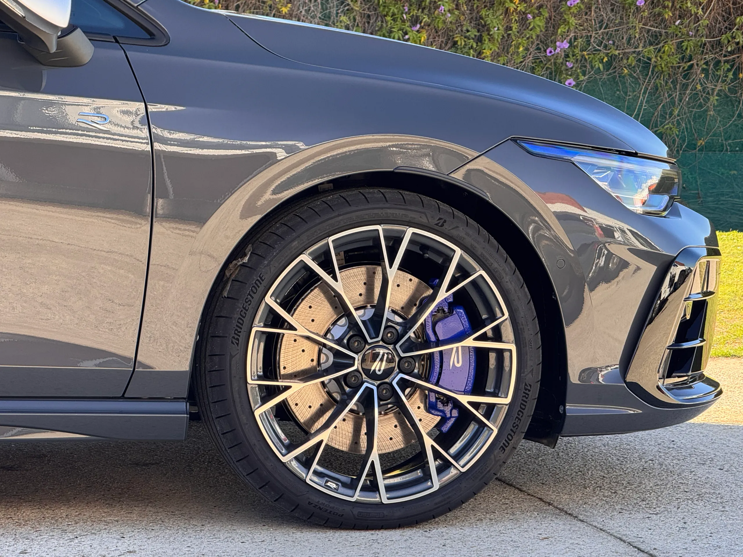Volkswagen Golf R front wheel, blue brake caliper and grey front guard outdoors