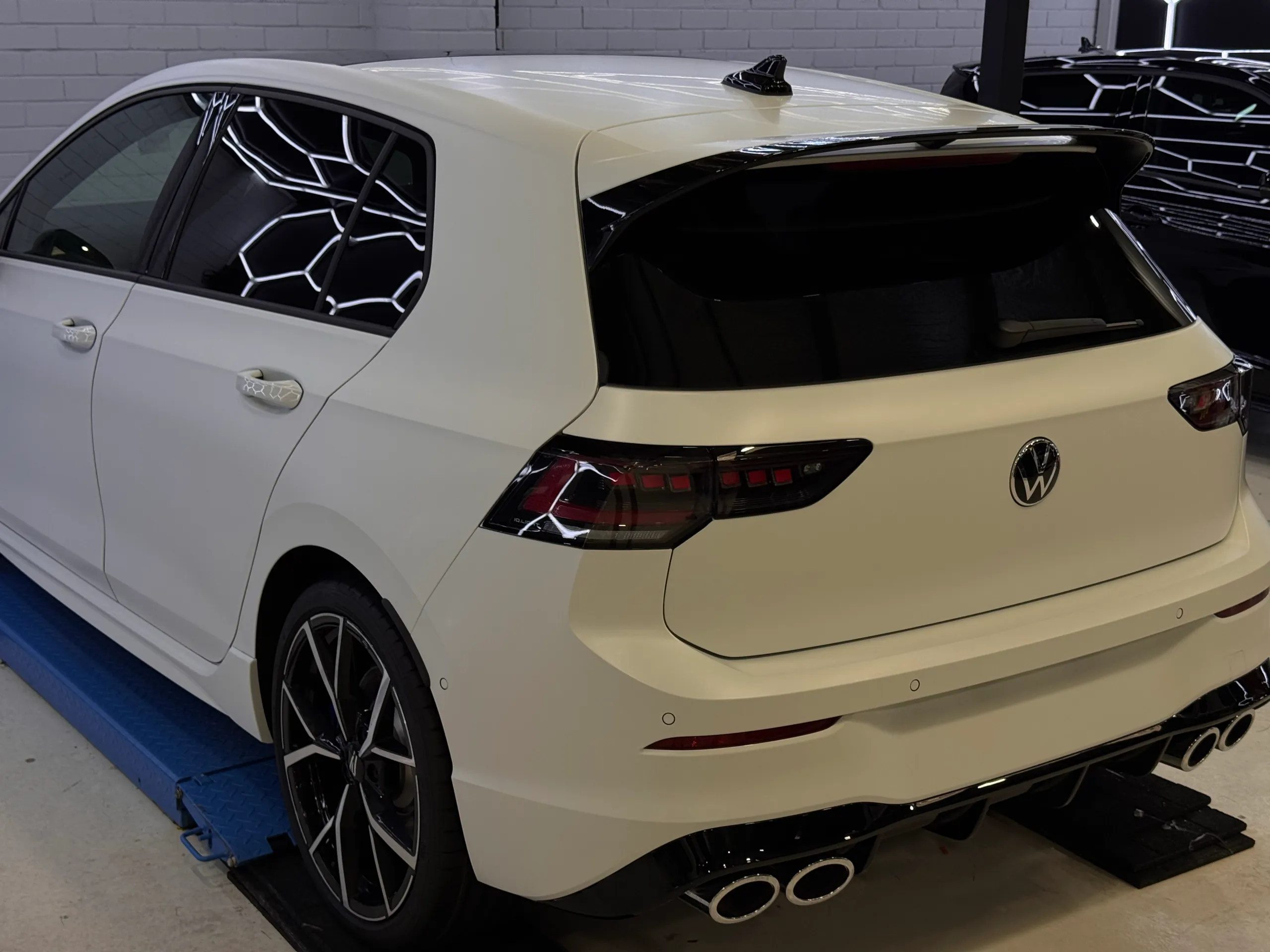 Matte white Volkswagen Golf R tailgate, rear quarter and four exhaust tips on a workshop lift