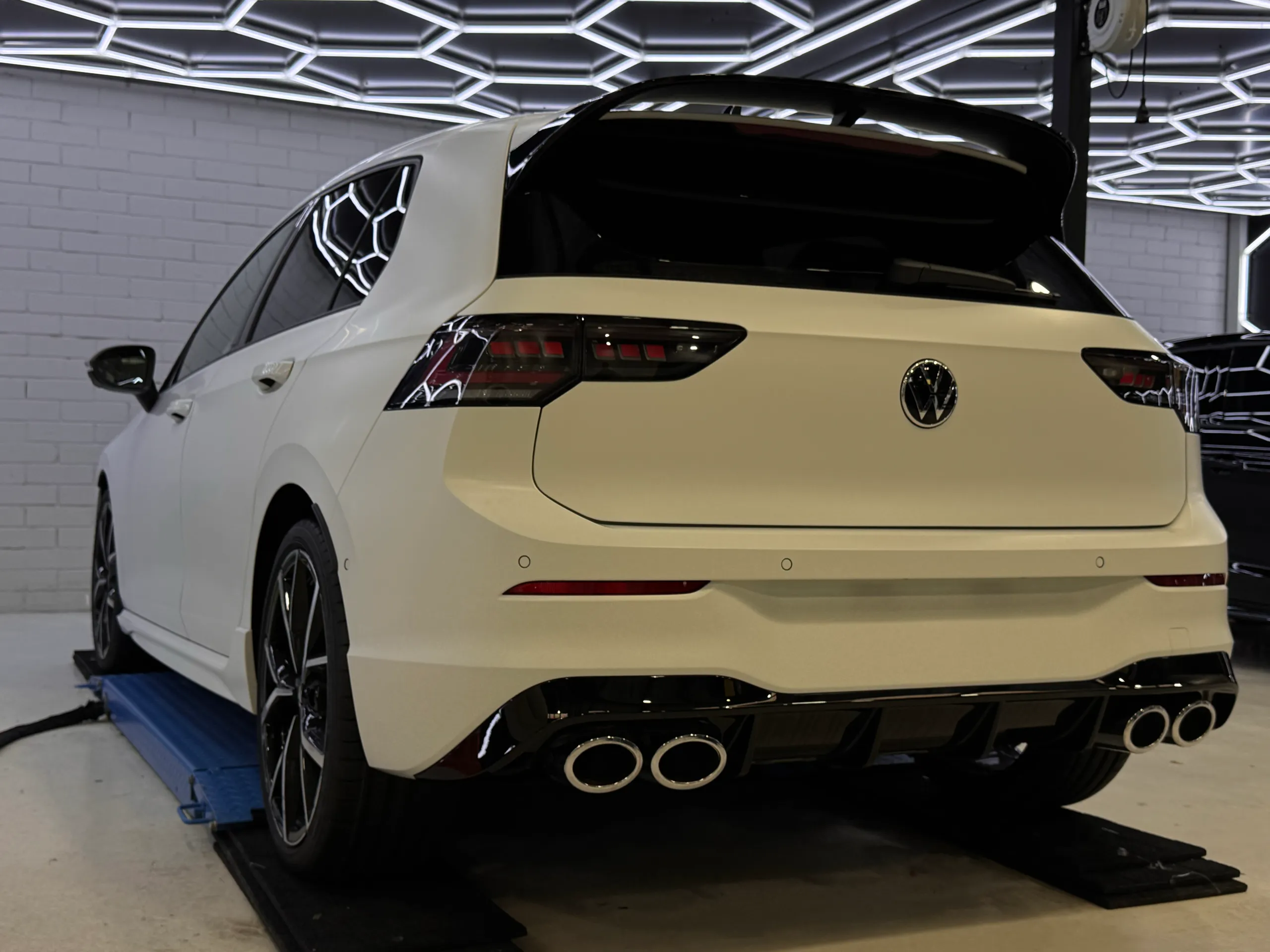 Matte white Volkswagen Golf R viewed from the rear quarter on a workshop lift