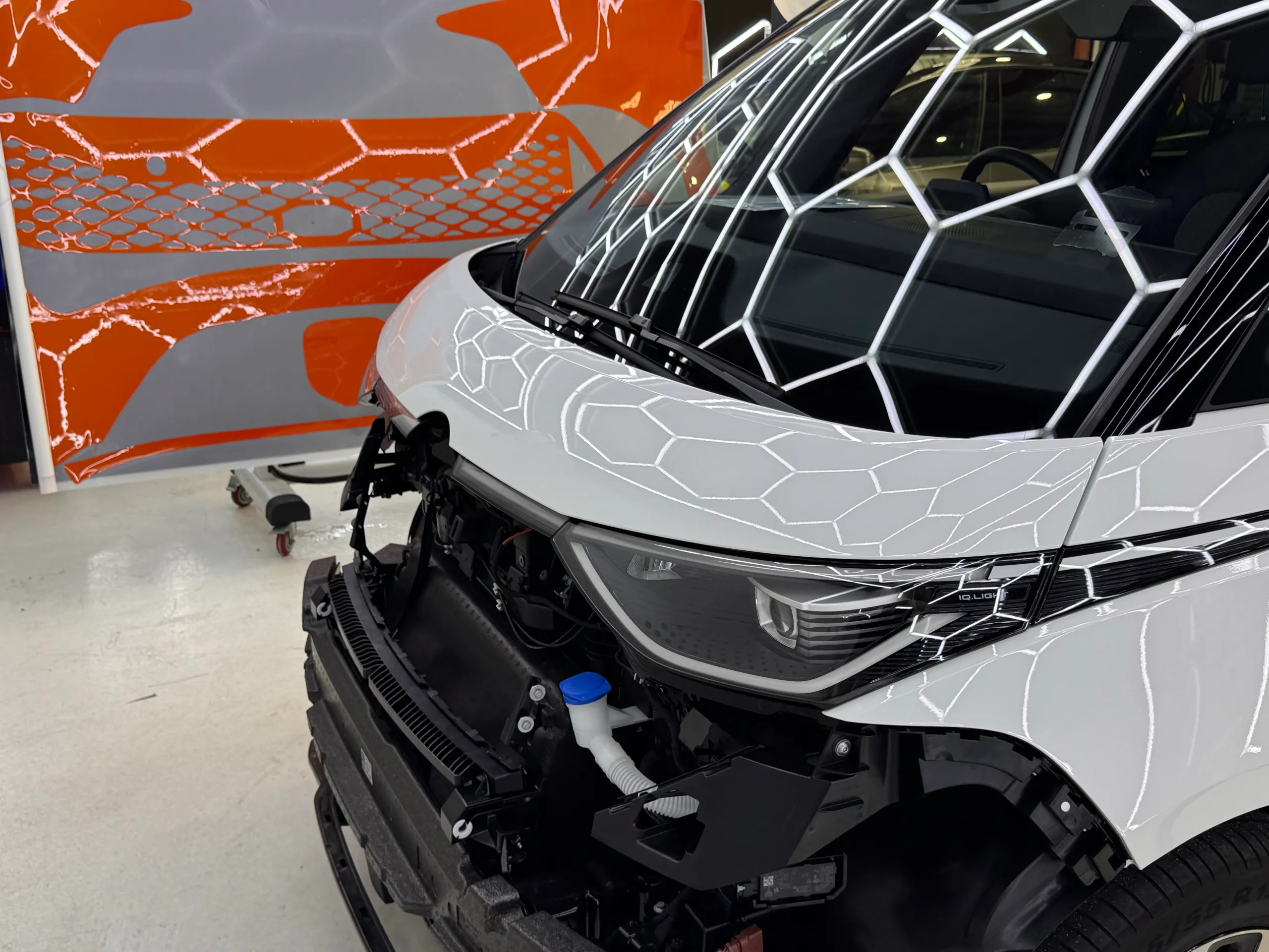 Volkswagen ID. Buzz front end with its bumper removed, beside orange cut film panels