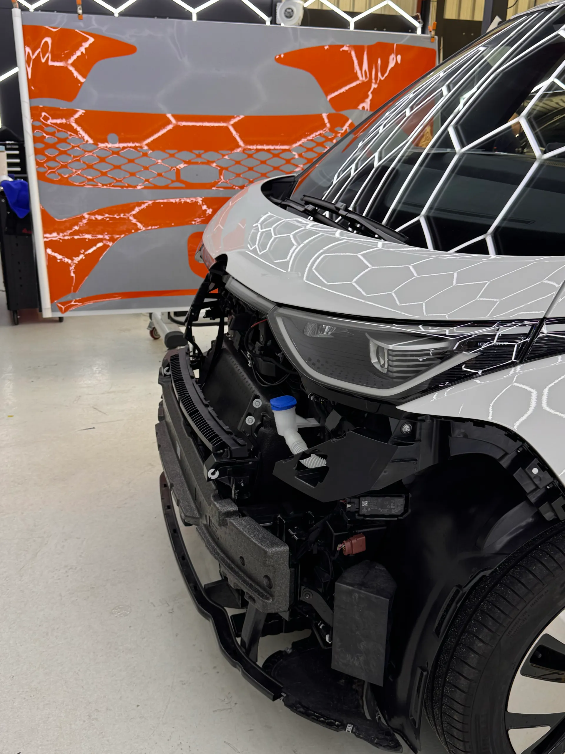 White Volkswagen ID. Buzz headlight and exposed front structure beside orange film panels