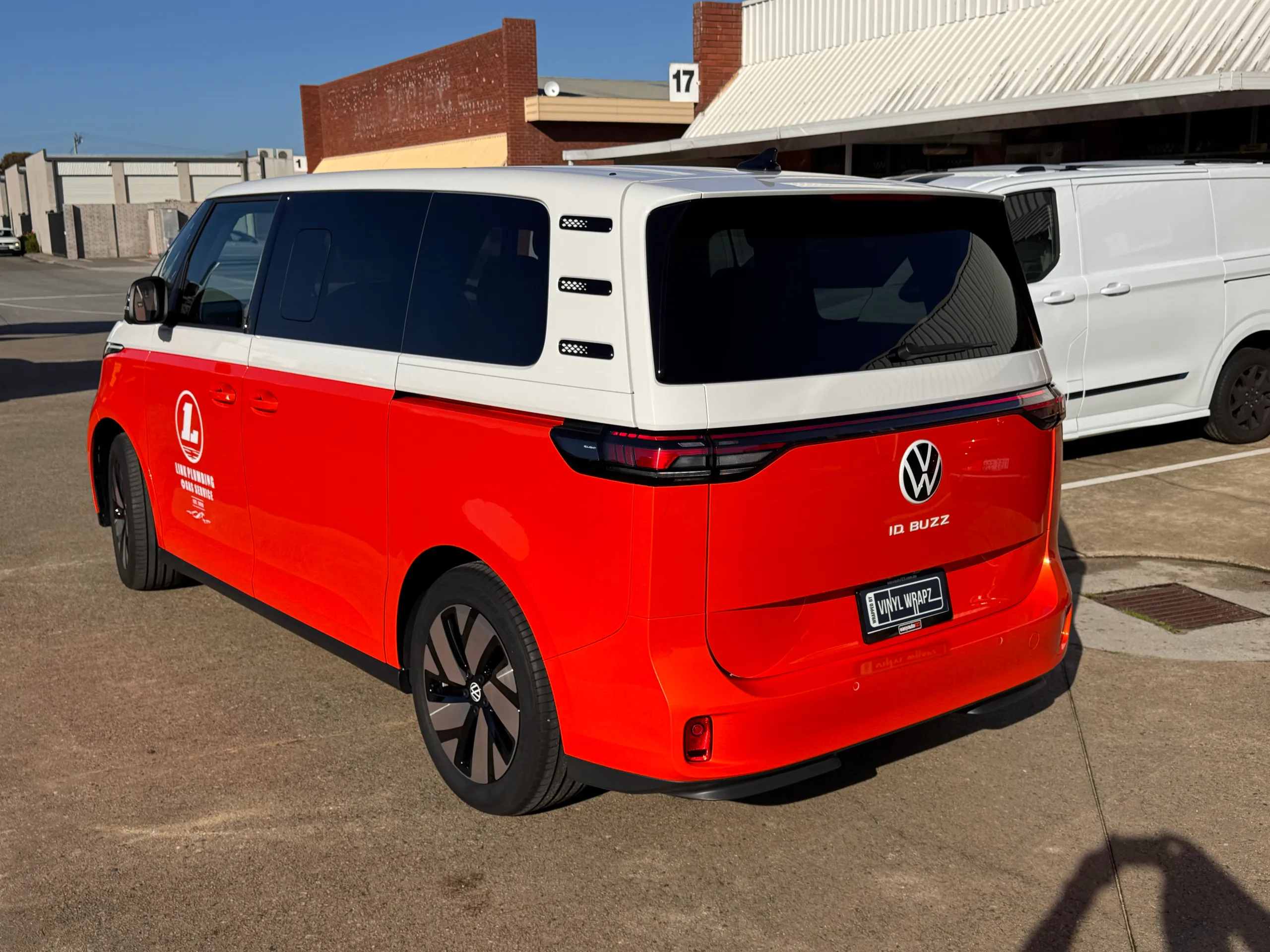 Rear-quarter view of an orange and white Volkswagen ID. Buzz outside the workshop