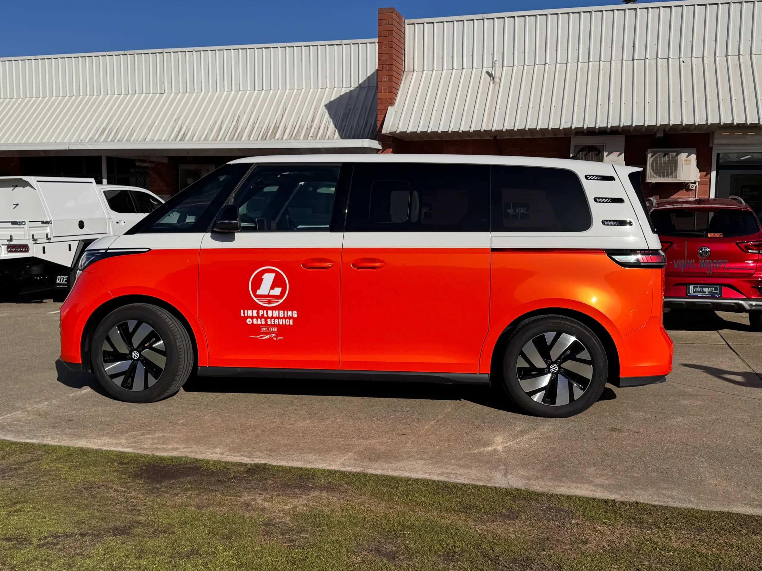 Orange and white Volkswagen ID. Buzz in side profile with Link Plumbing Gas Service branding