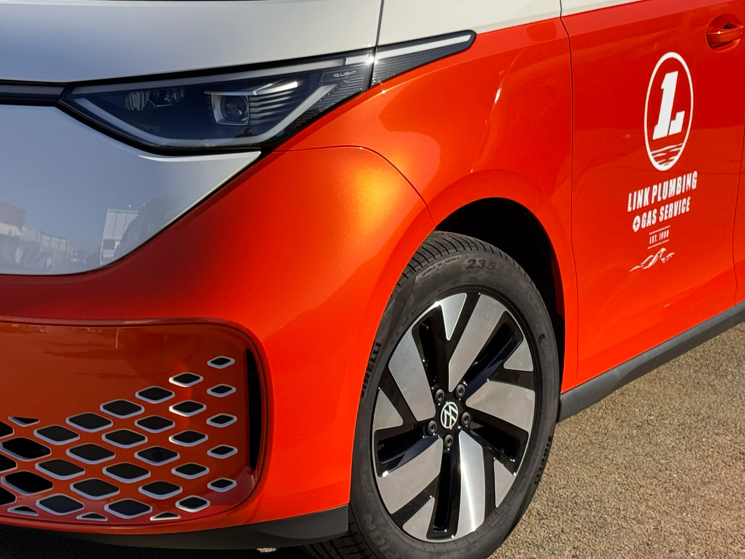 Orange Volkswagen ID. Buzz front guard and wheel beside Link Plumbing branding on the door