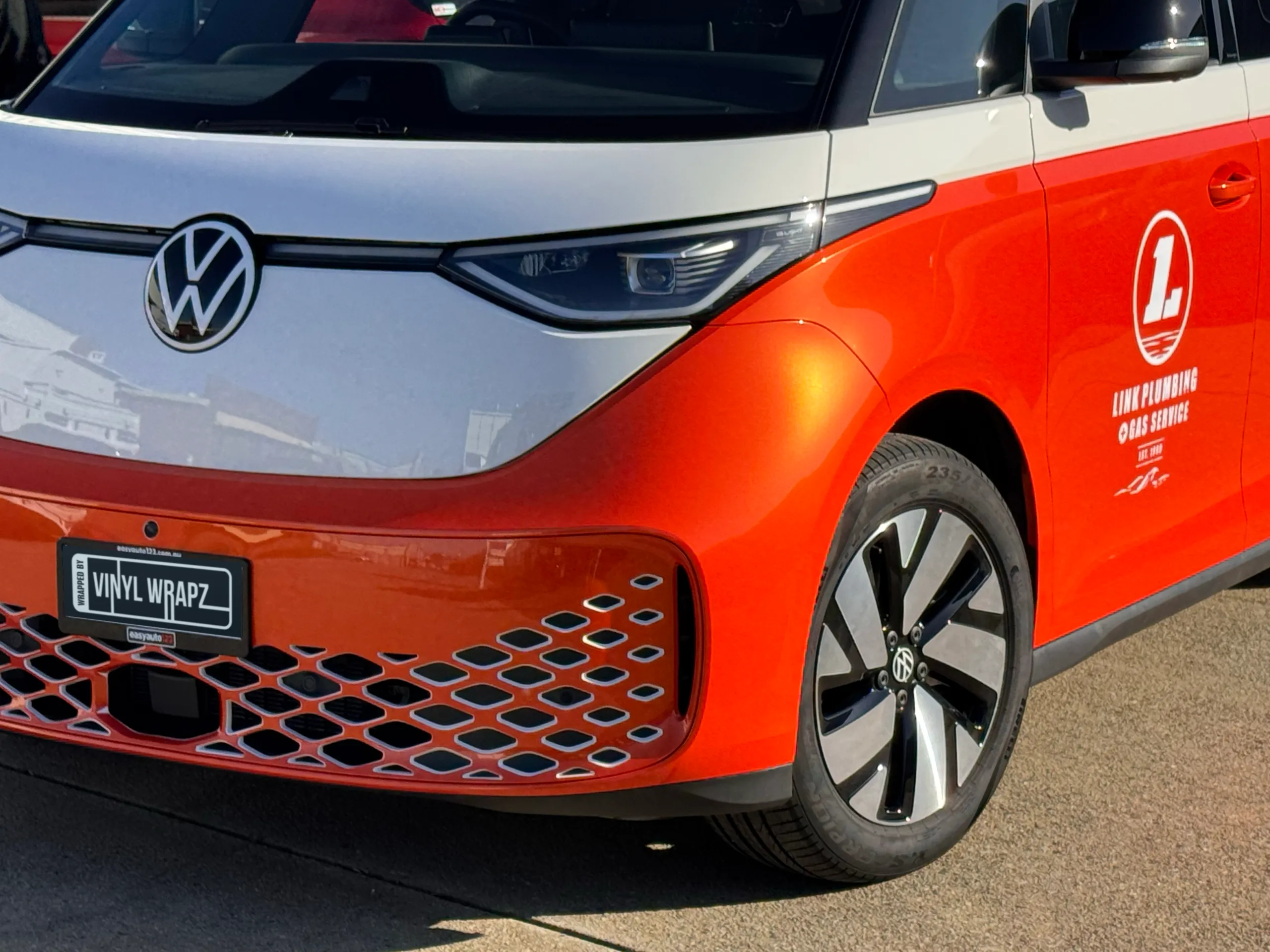 Orange and white Volkswagen ID. Buzz front quarter showing its VW emblem and Link Plumbing door logo