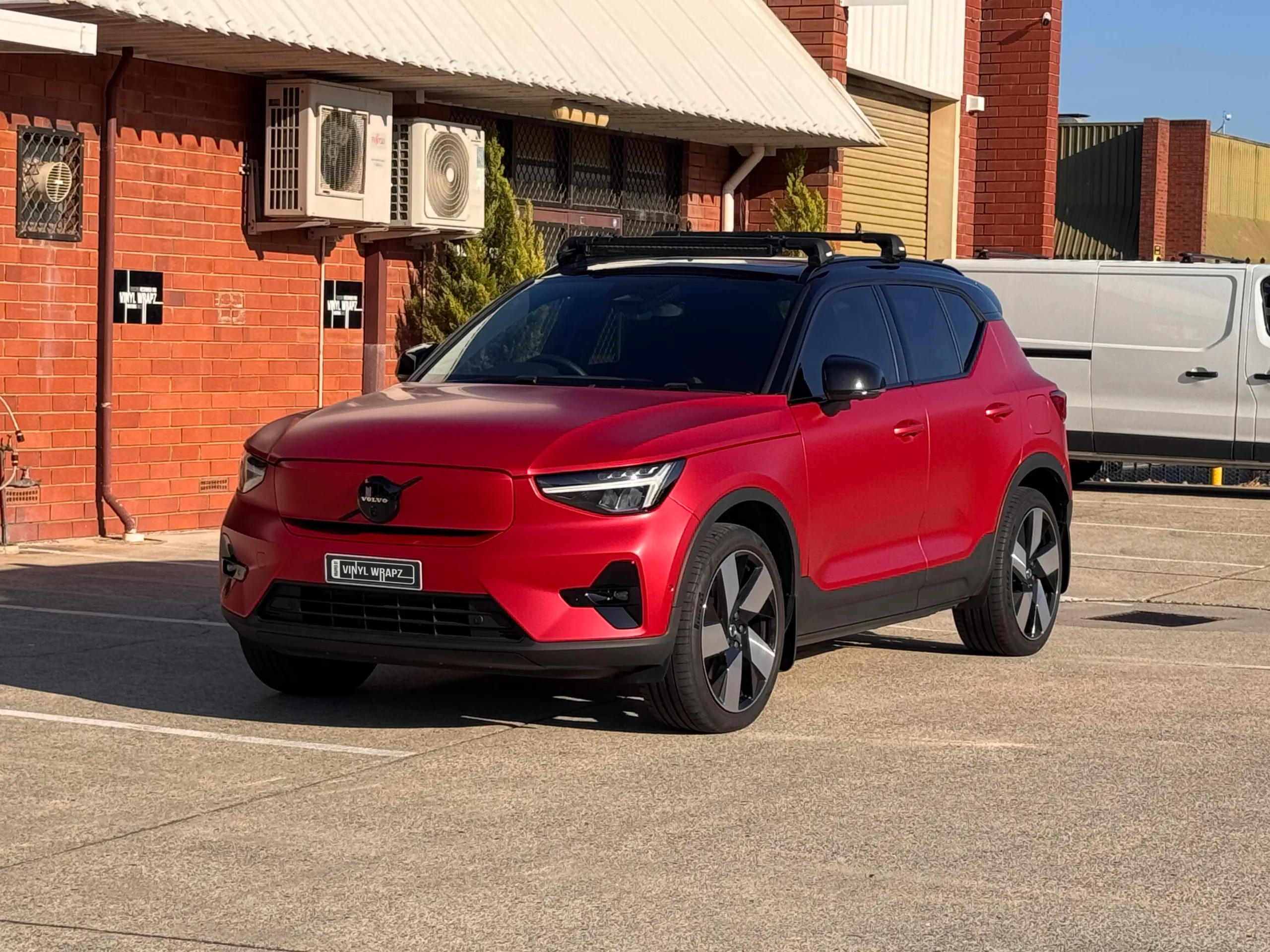 Red Volvo XC40 with a black roof parked outside a brick workshop