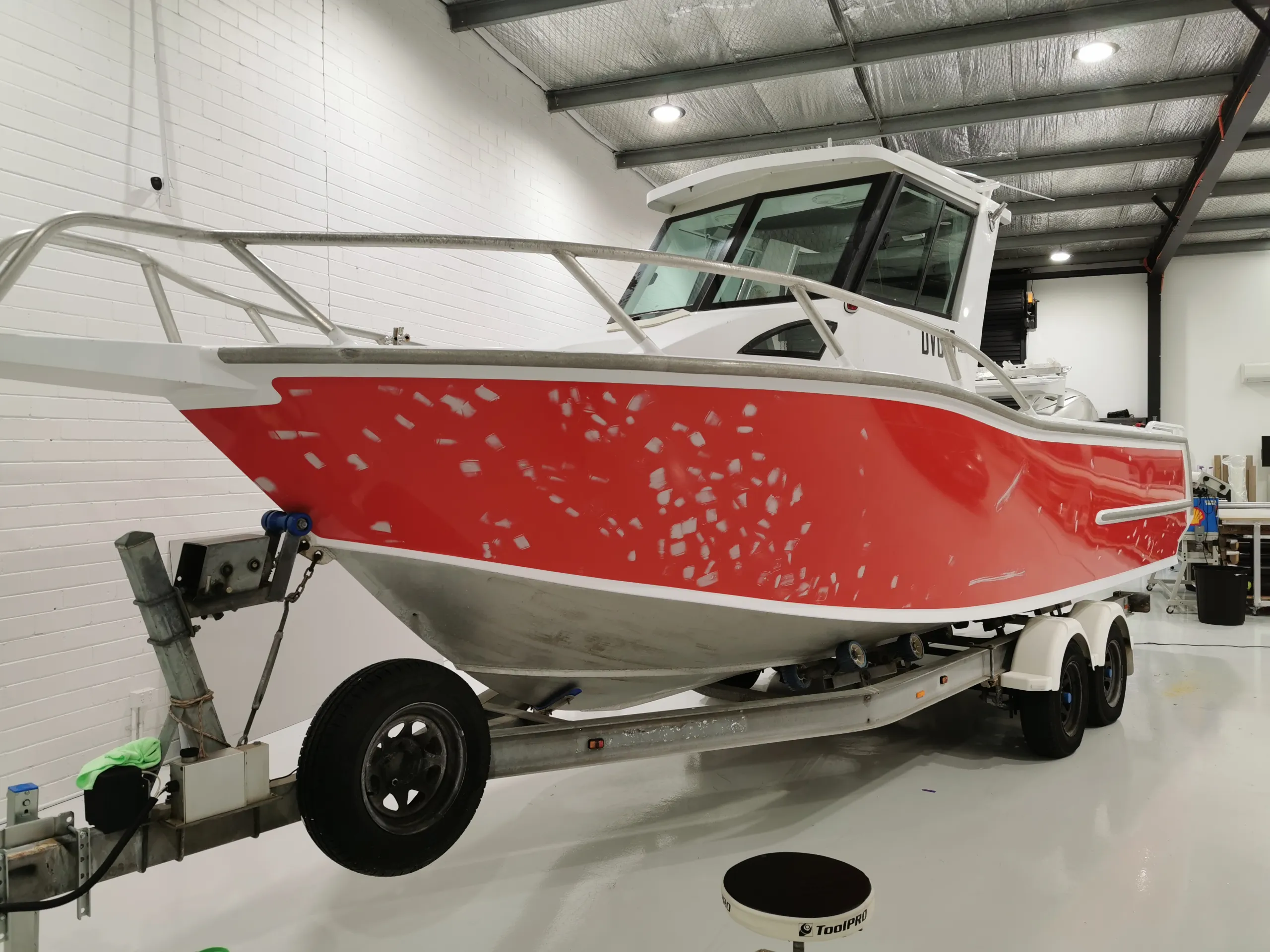 Orange boat hull with sanded patches on a trailer before the charcoal colour change