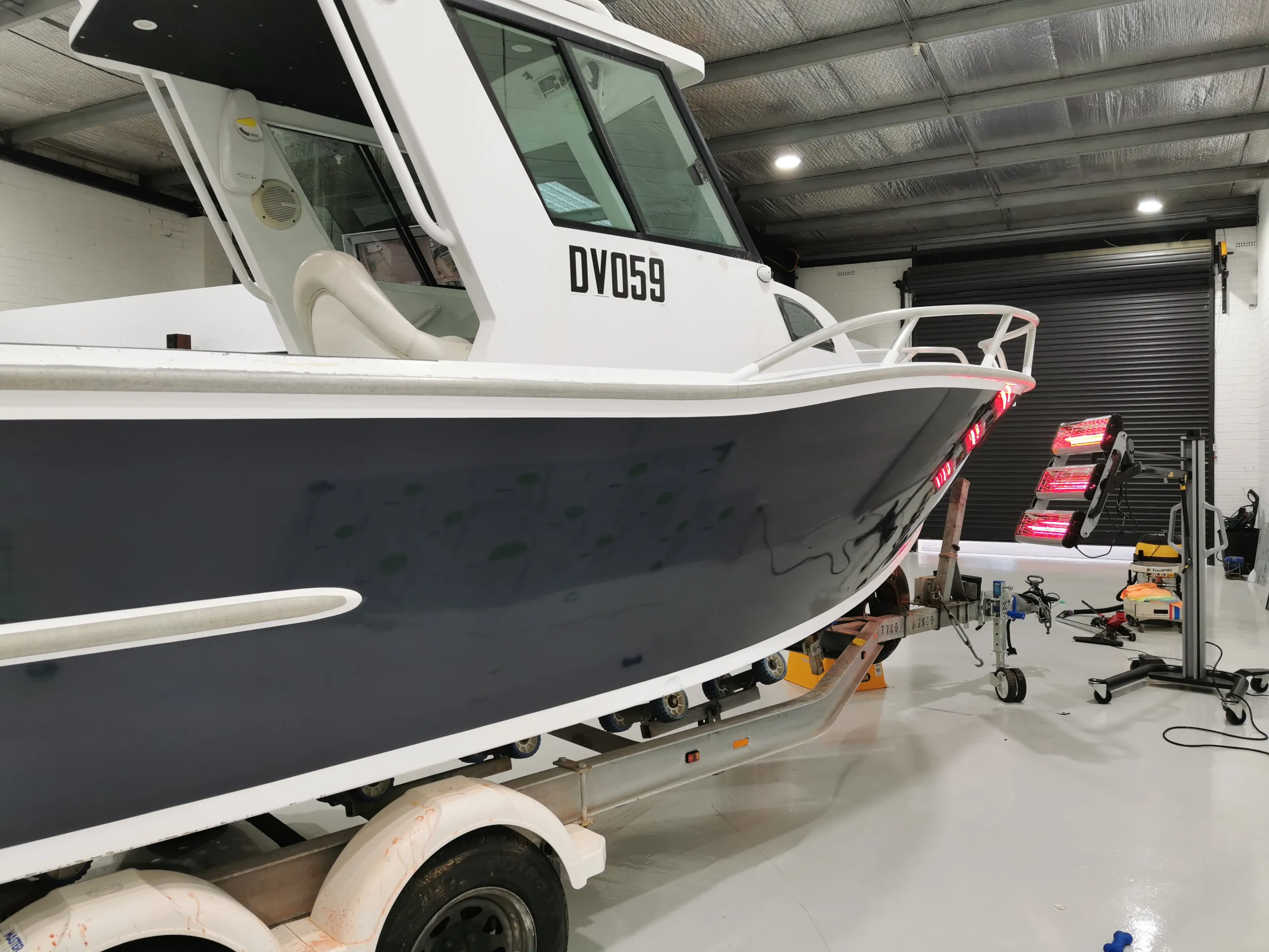 Close side view of the charcoal boat hull and white cabin inside the workshop