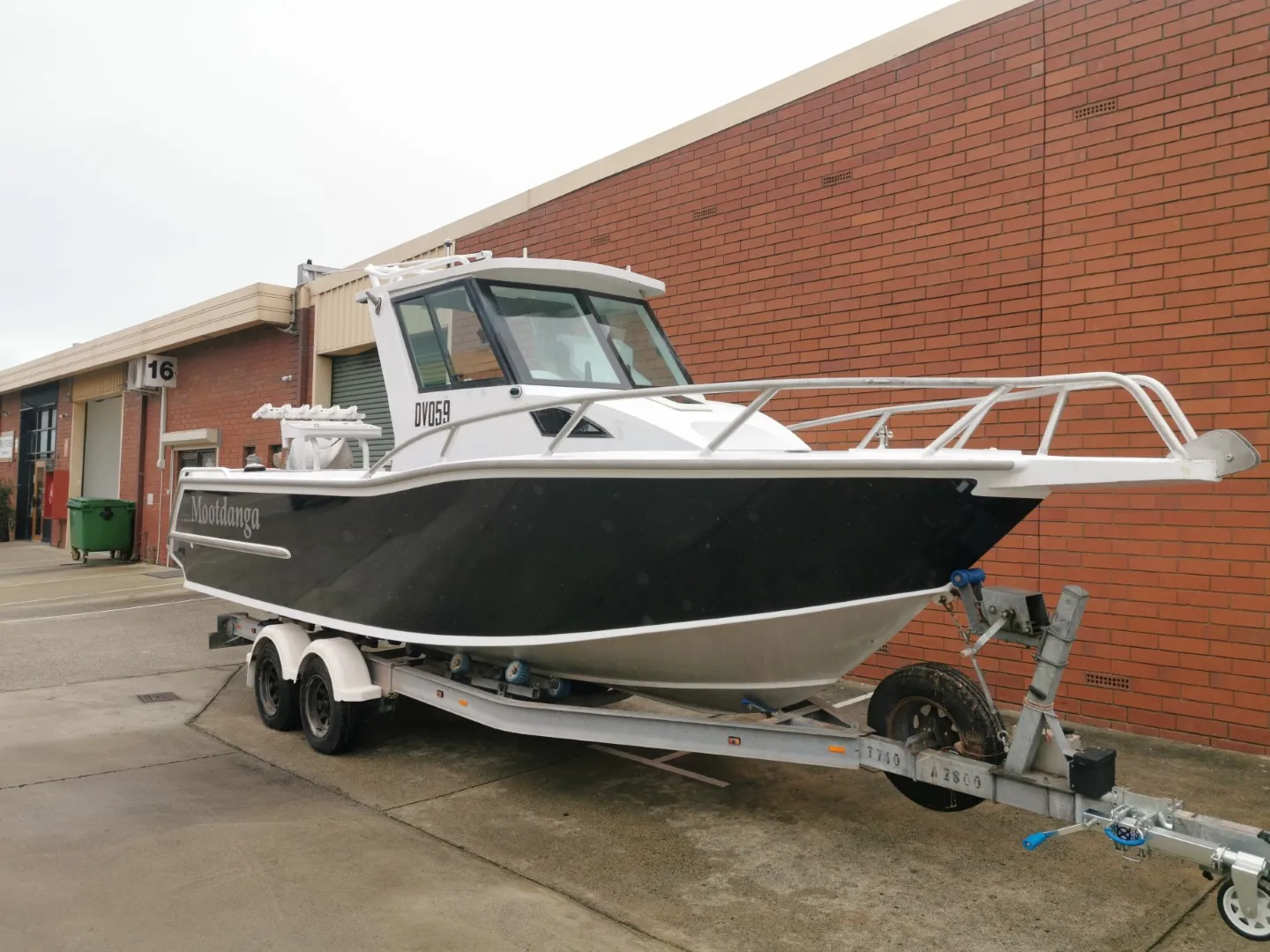 Charcoal boat with white trim on its trailer outside a brick workshop
