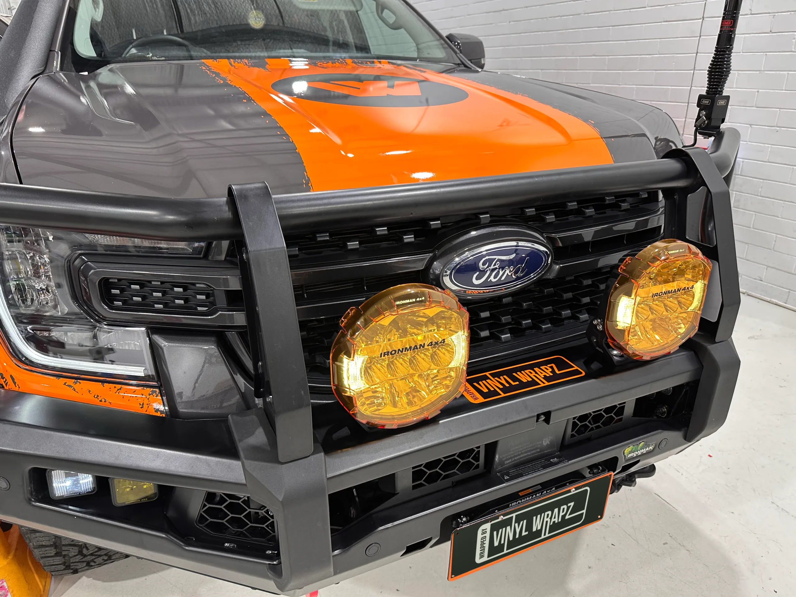 Ford Ranger bonnet with an orange Wildtrak logo stripe behind a bull bar and yellow driving lights