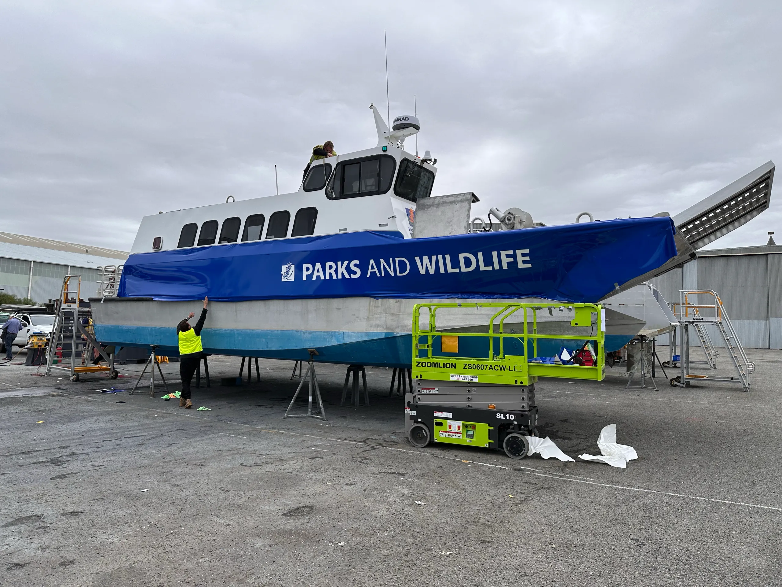Workers fitting blue Parks and Wildlife graphics along the vessel on a hardstand