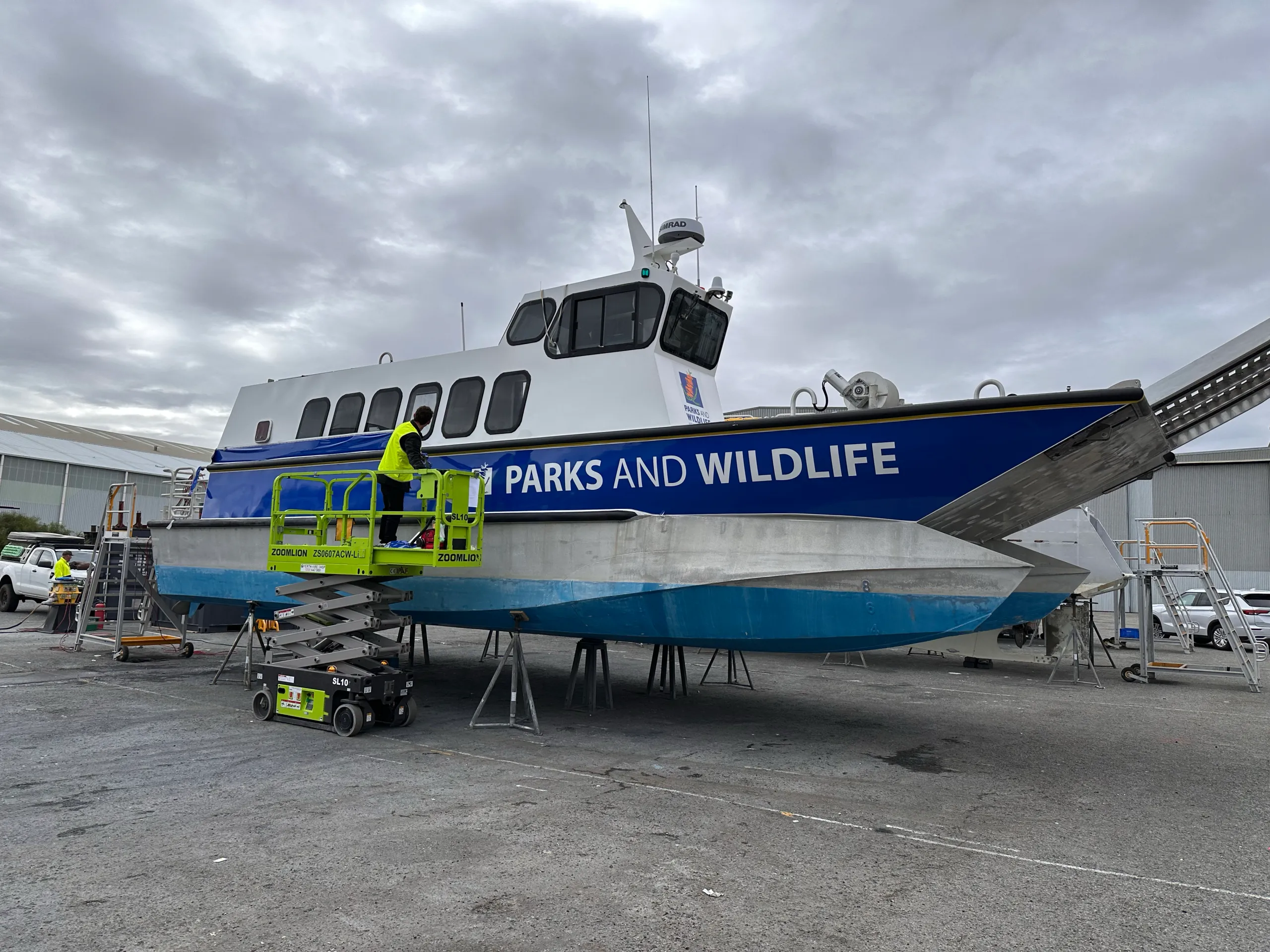 Installer on a scissor lift fitting blue Parks and Wildlife graphics to the vessel side