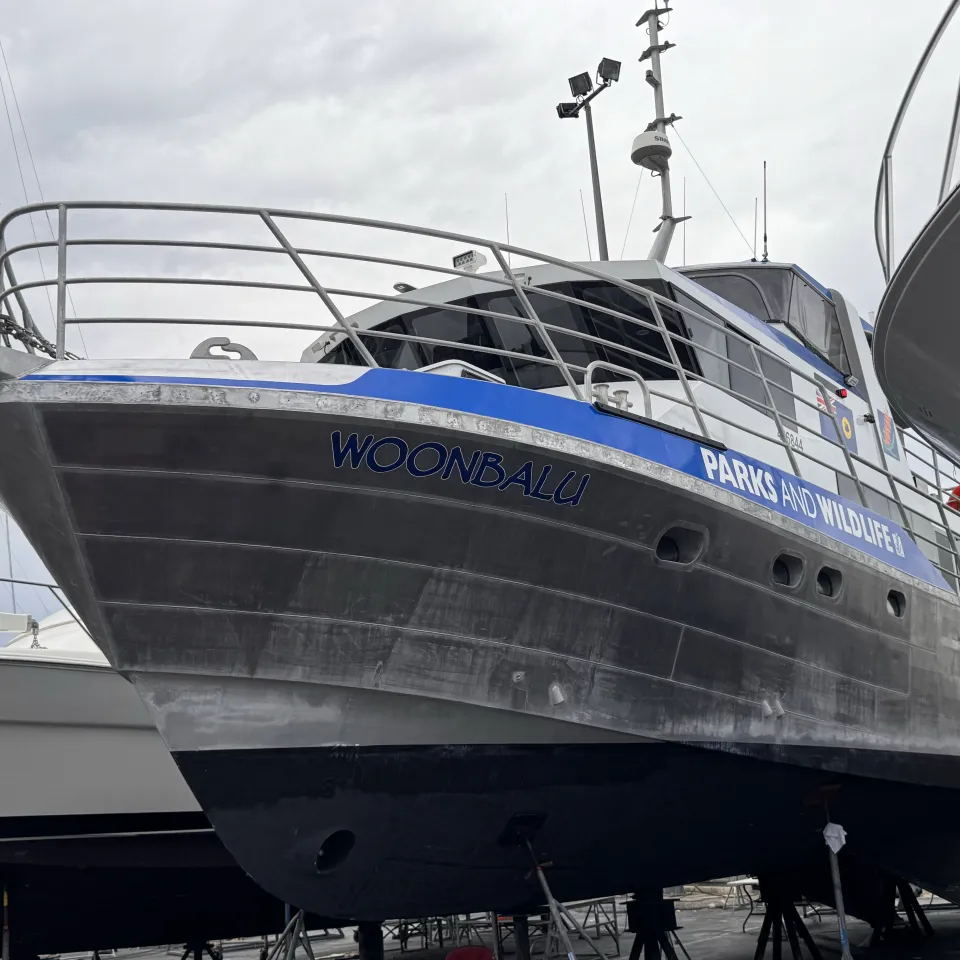 Woonbalu on boatyard stands with blue Parks and Wildlife branding along its bow and cabin