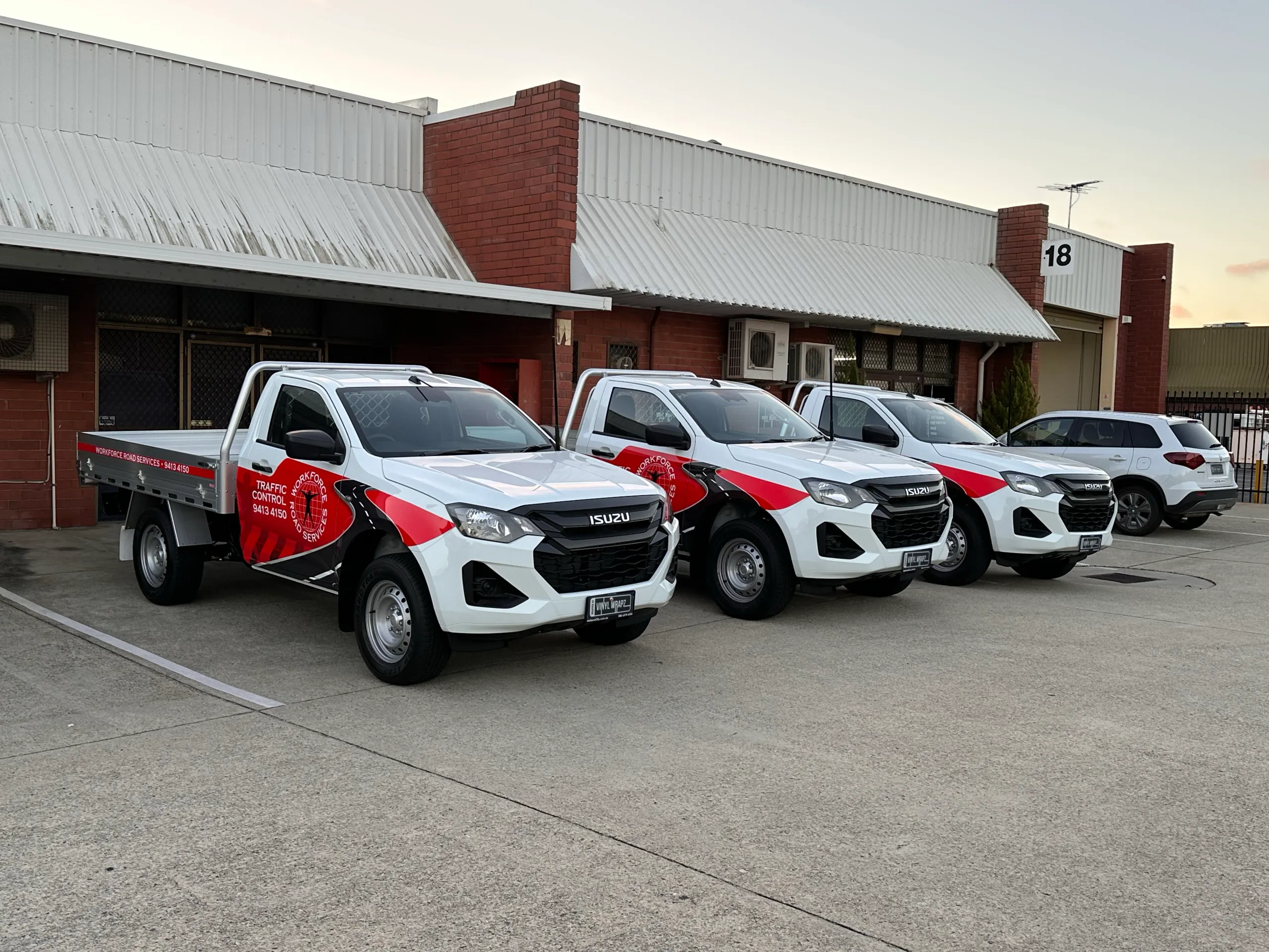 Three white Isuzu traffic control utes with matching Workforce Road Services graphics at dusk