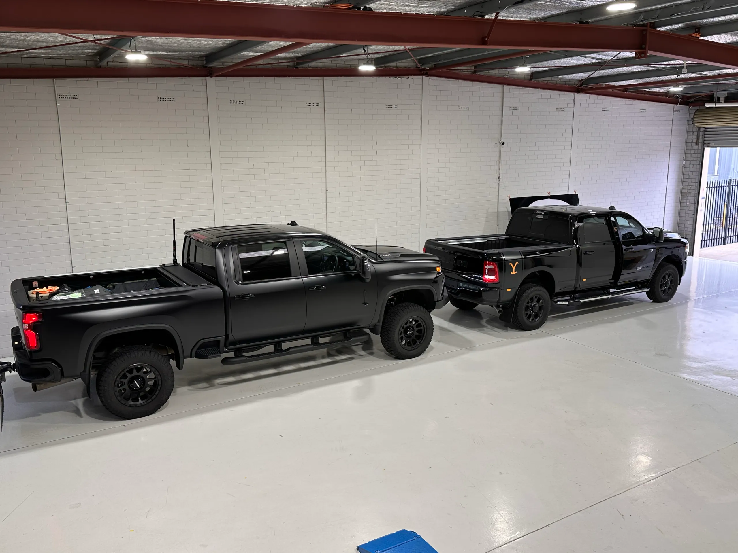 Two black pickup trucks with contrasting satin and gloss finishes parked in the workshop