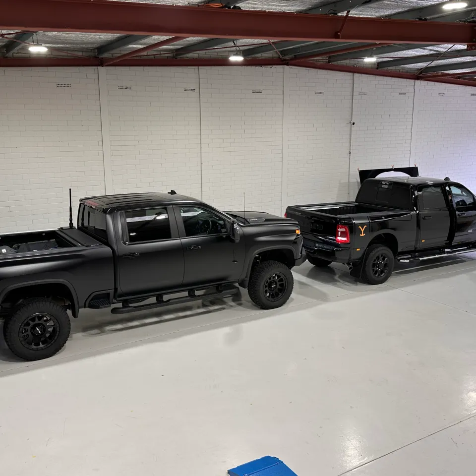Two black pickup trucks with contrasting satin and gloss finishes parked in the workshop