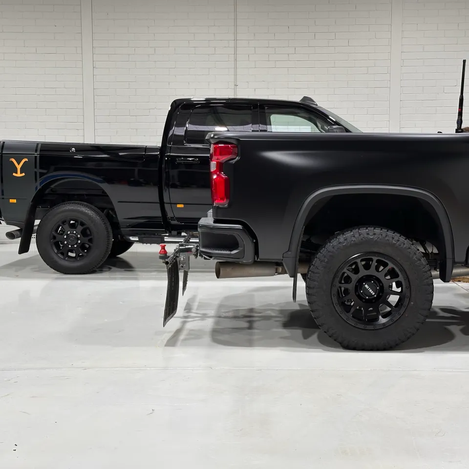 Rear quarters of satin and gloss black pickup trucks parked side by side
