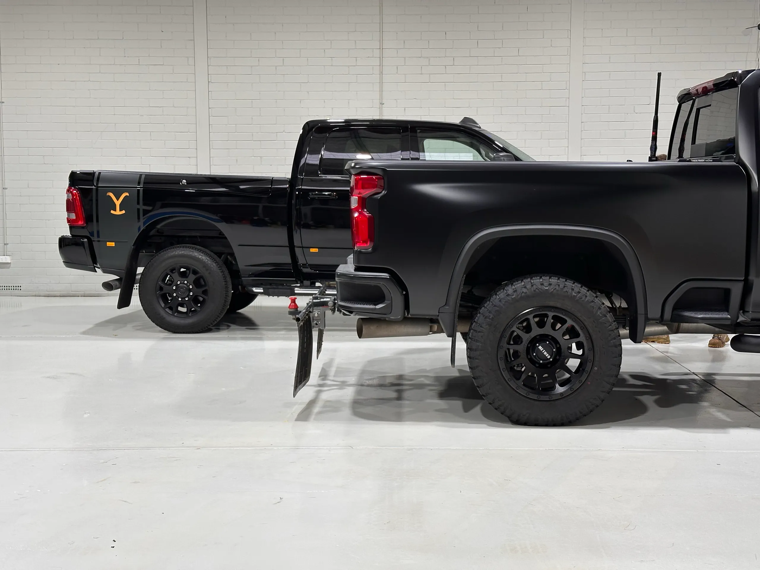 Rear quarters of satin and gloss black pickup trucks parked side by side