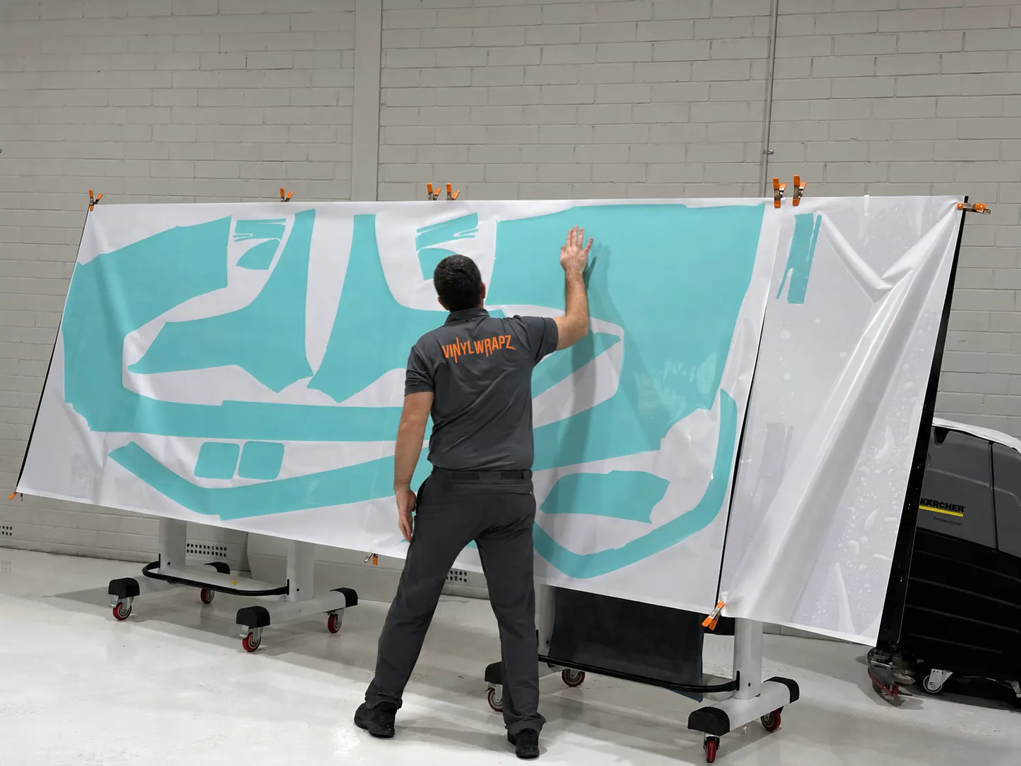 Installer, back to camera, checking cut and weeded paint protection film templates hung on rolling stands