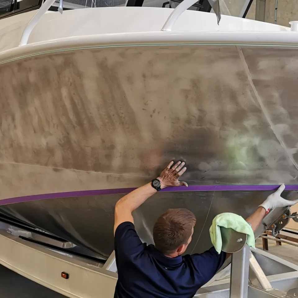 Installer facing away while preparing a bare aluminium boat hull along masking tape