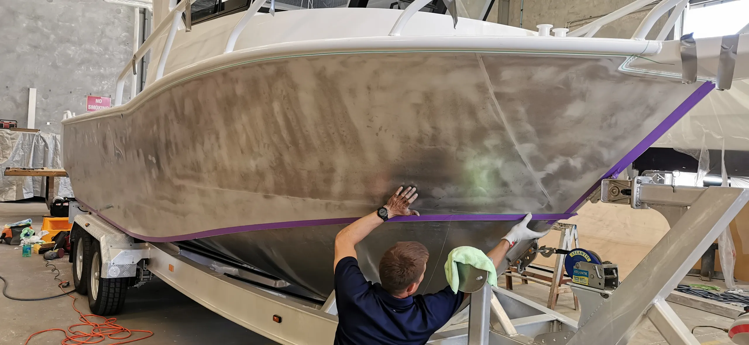 Installer facing away while preparing a bare aluminium boat hull along masking tape