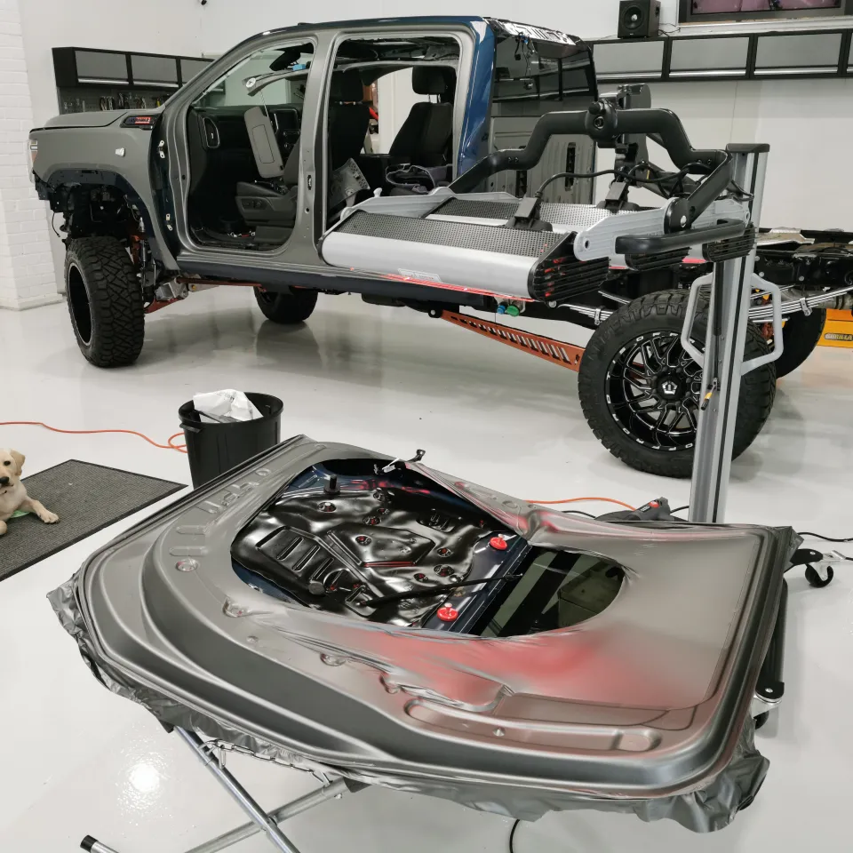Dismantled ute cab and removed door on a workshop stand, with a dog nearby